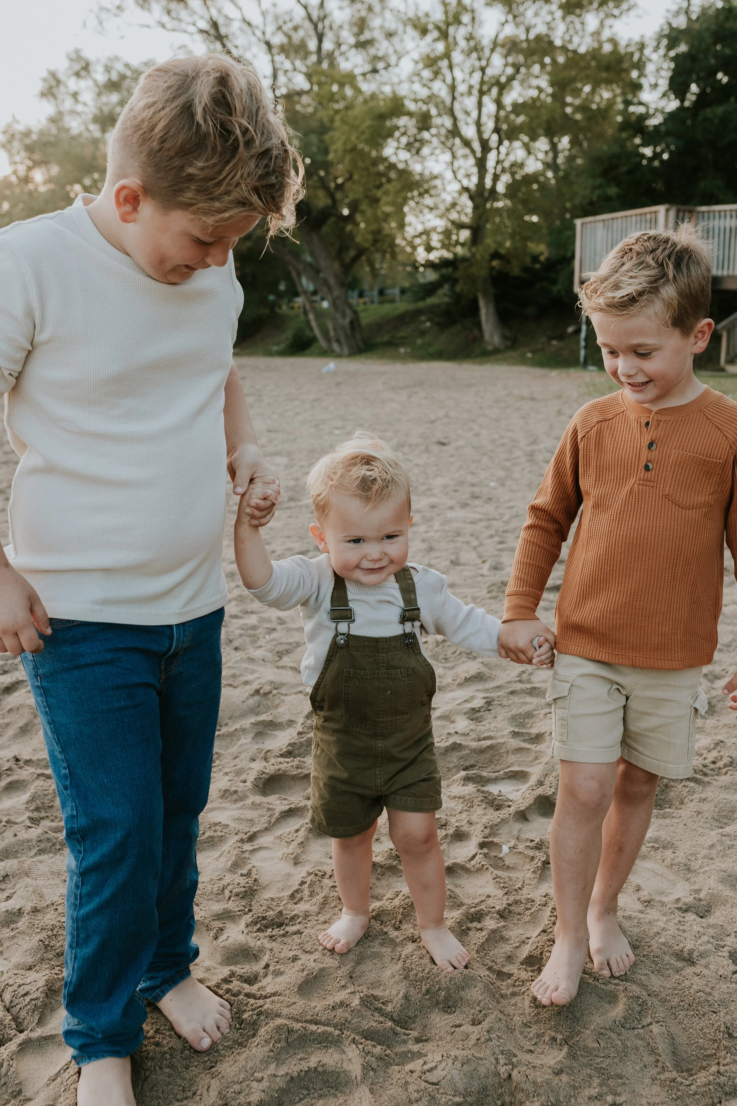 3 young brothers walking hand in hand barefoot during family photos at de la salle beach in georgina ontario