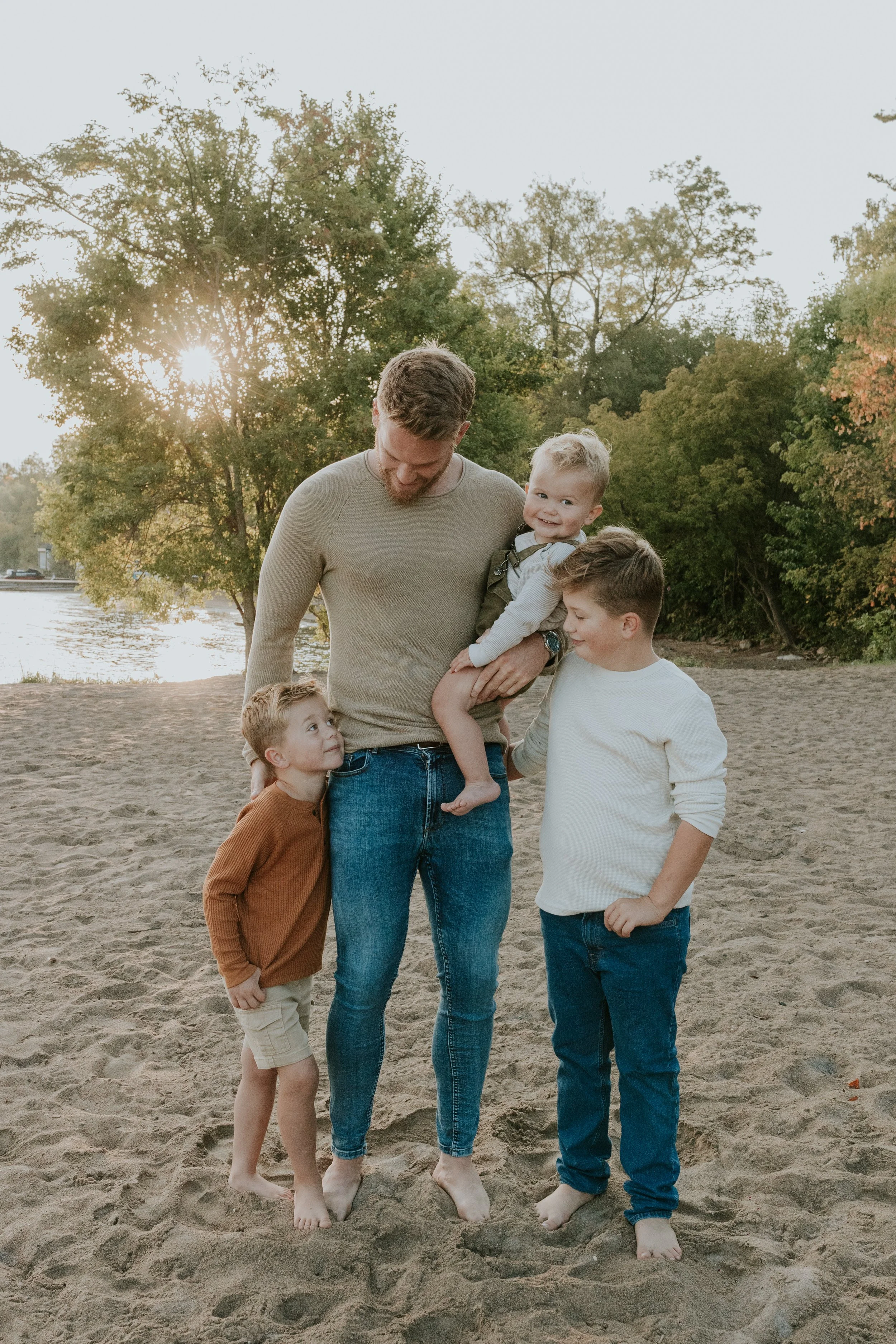 father and 3 young sons cuddled up during family photos at de la salle beach in georgina ontario