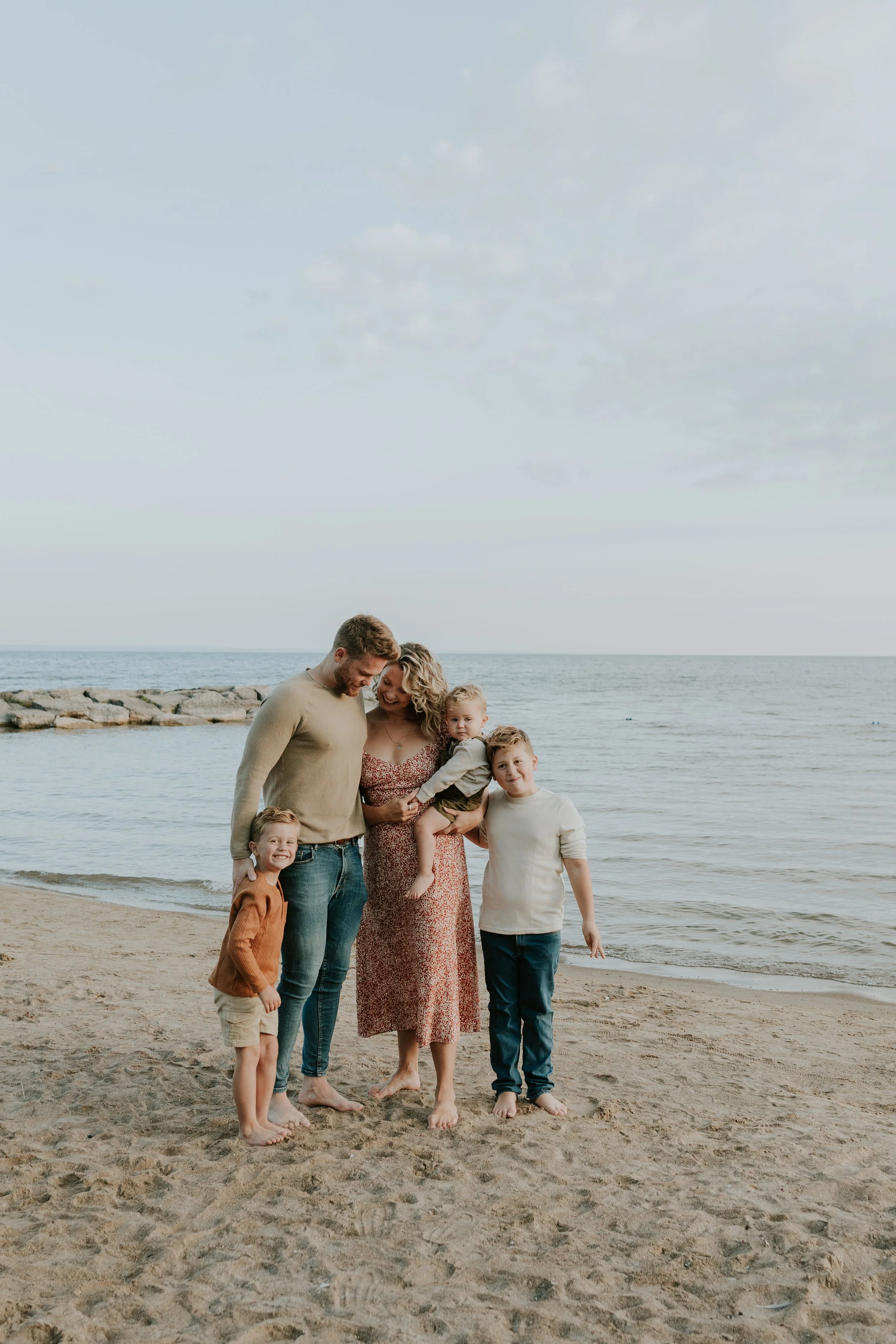young family stood infront of lake simcoe at de la salle beach in georgina ontario cuddled up at sunrise for family photos
