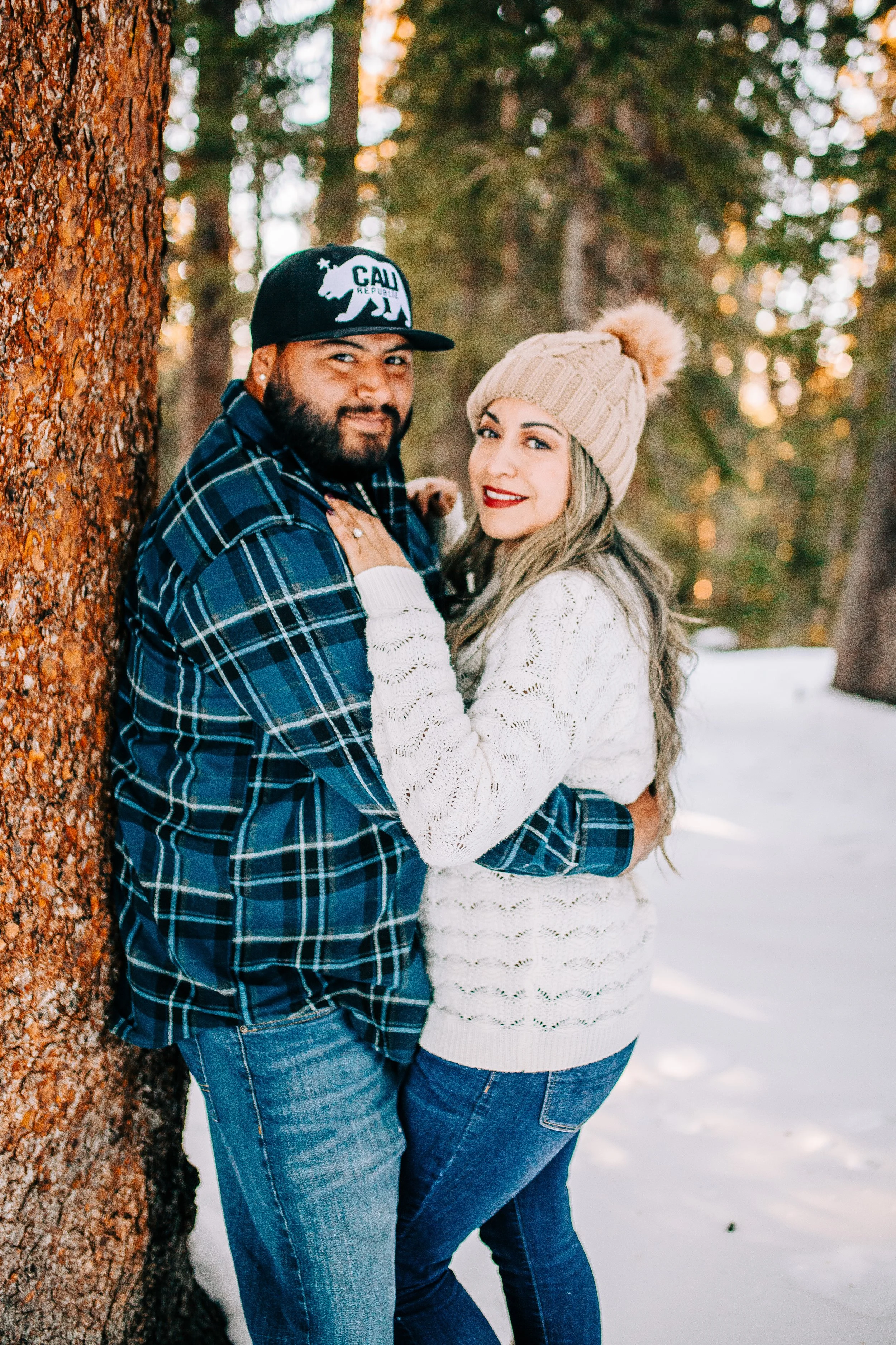 Man and woman standing next to tree in snow