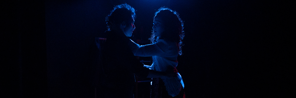Silhouettes of a man and a woman facing each other in a dark setting with blue lighting.