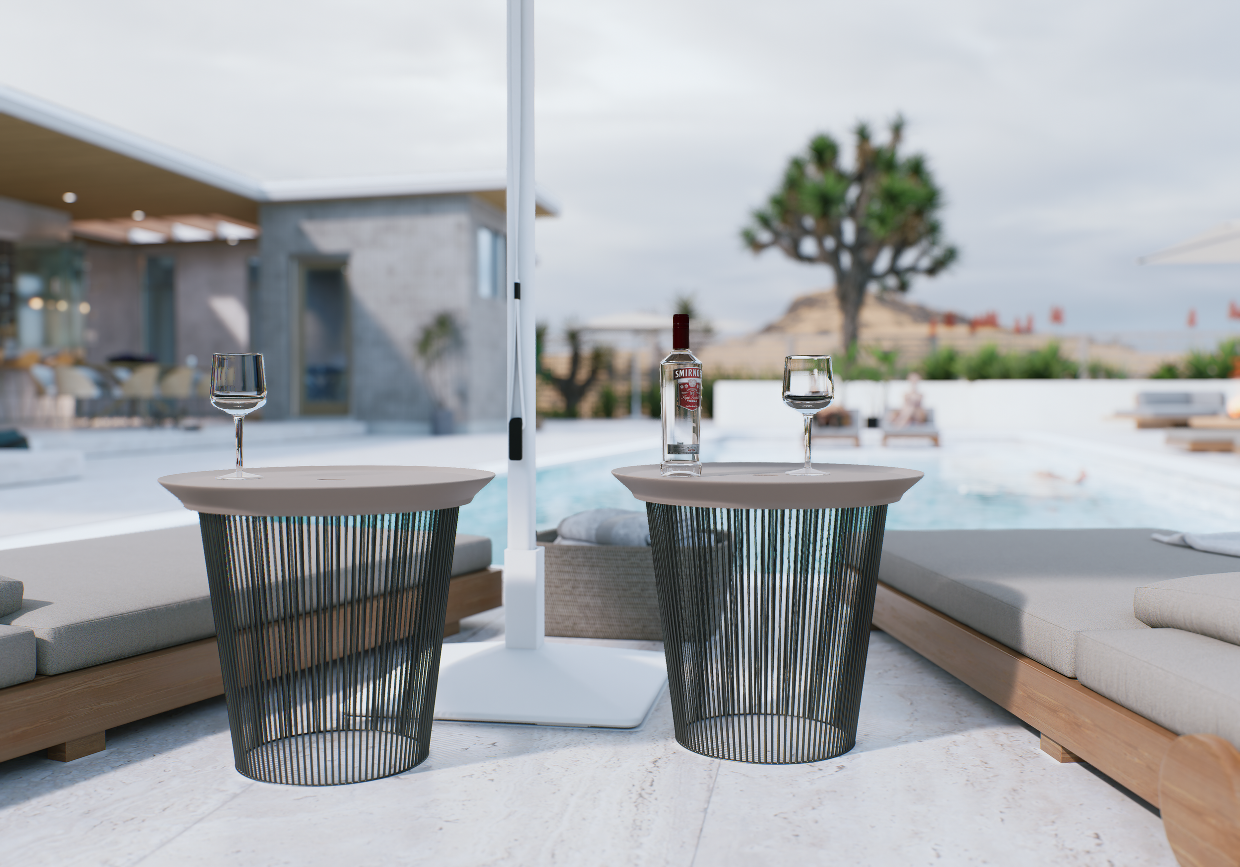Outdoor patio with two round tables each with two empty wine glasses and a bottle of Smirnoff vodka, surrounding modern lounge chairs and cushioned seating with a view of a tree and a building in the background.