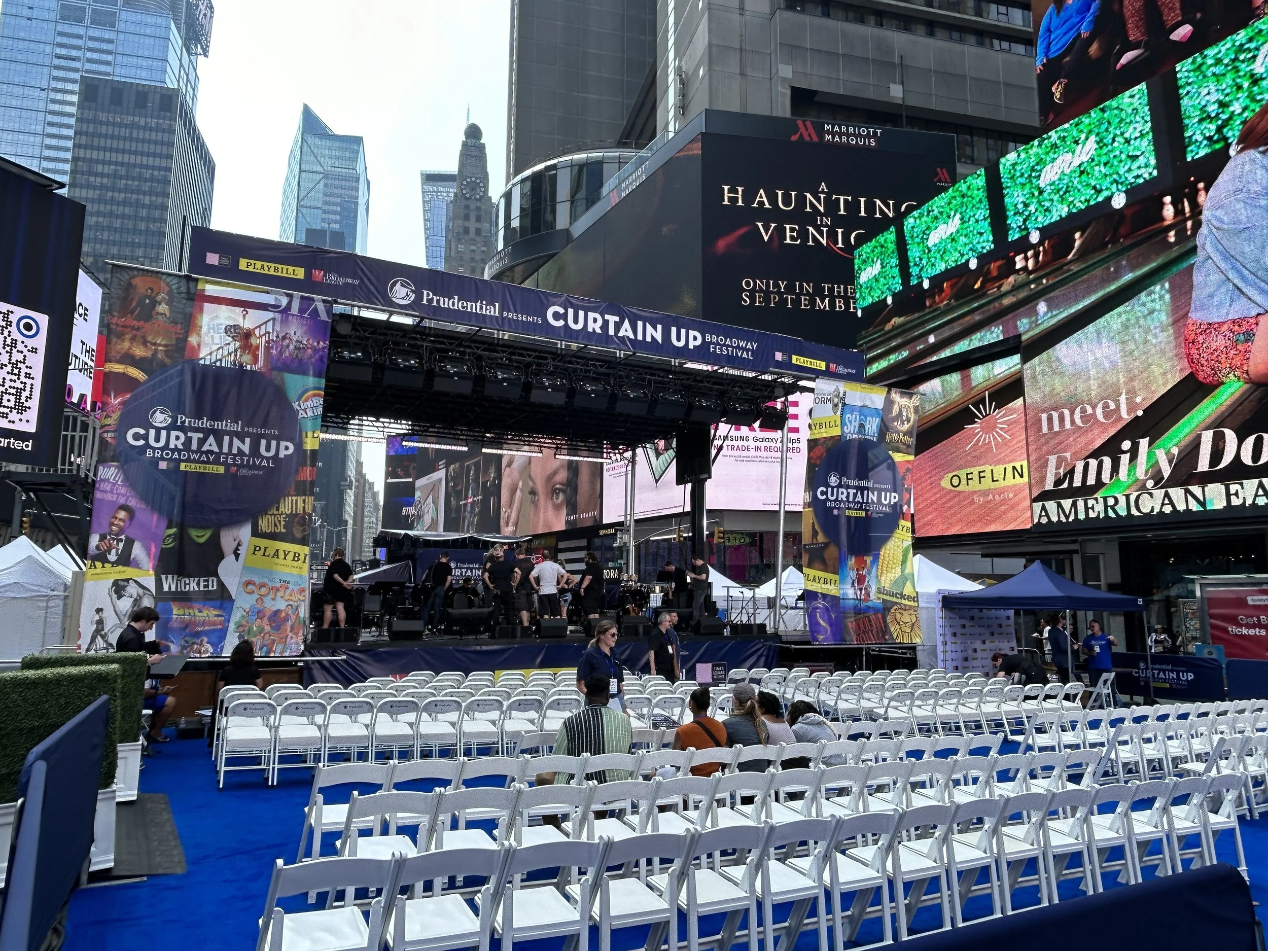 A Pride-themed float with rainbow curtains and decorations, displaying a yellow Playbill banner that reads 'Proudly celebrating equity and love for all,' in Times Square, New York City.