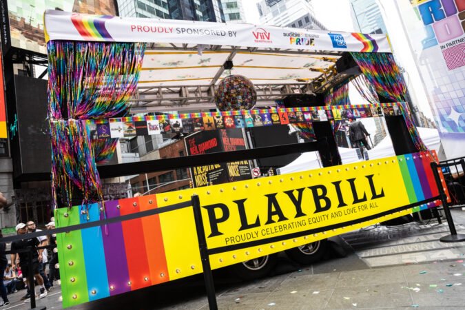 A Pride-themed float with rainbow curtains and decorations, displaying a yellow Playbill banner that reads 'Proudly celebrating equity and love for all,' in Times Square, New York City.
