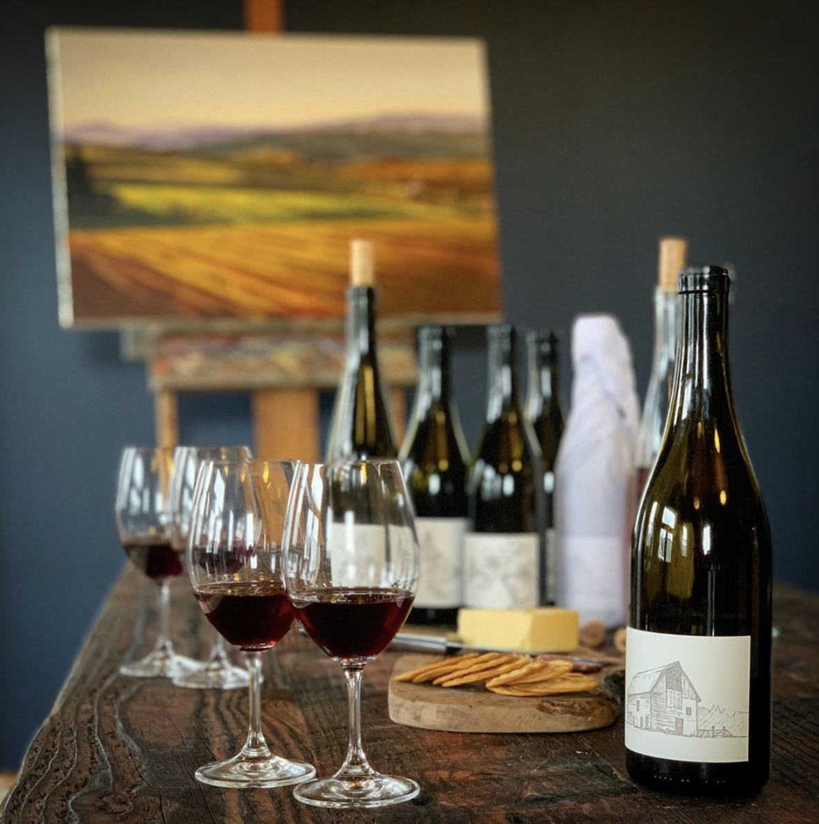  A wine tasting at the Big Table Farm Atelier in Carlton, OR. Wine and cheese plate on a table with a beautiful landscape painting by Clare Carver in the background. 