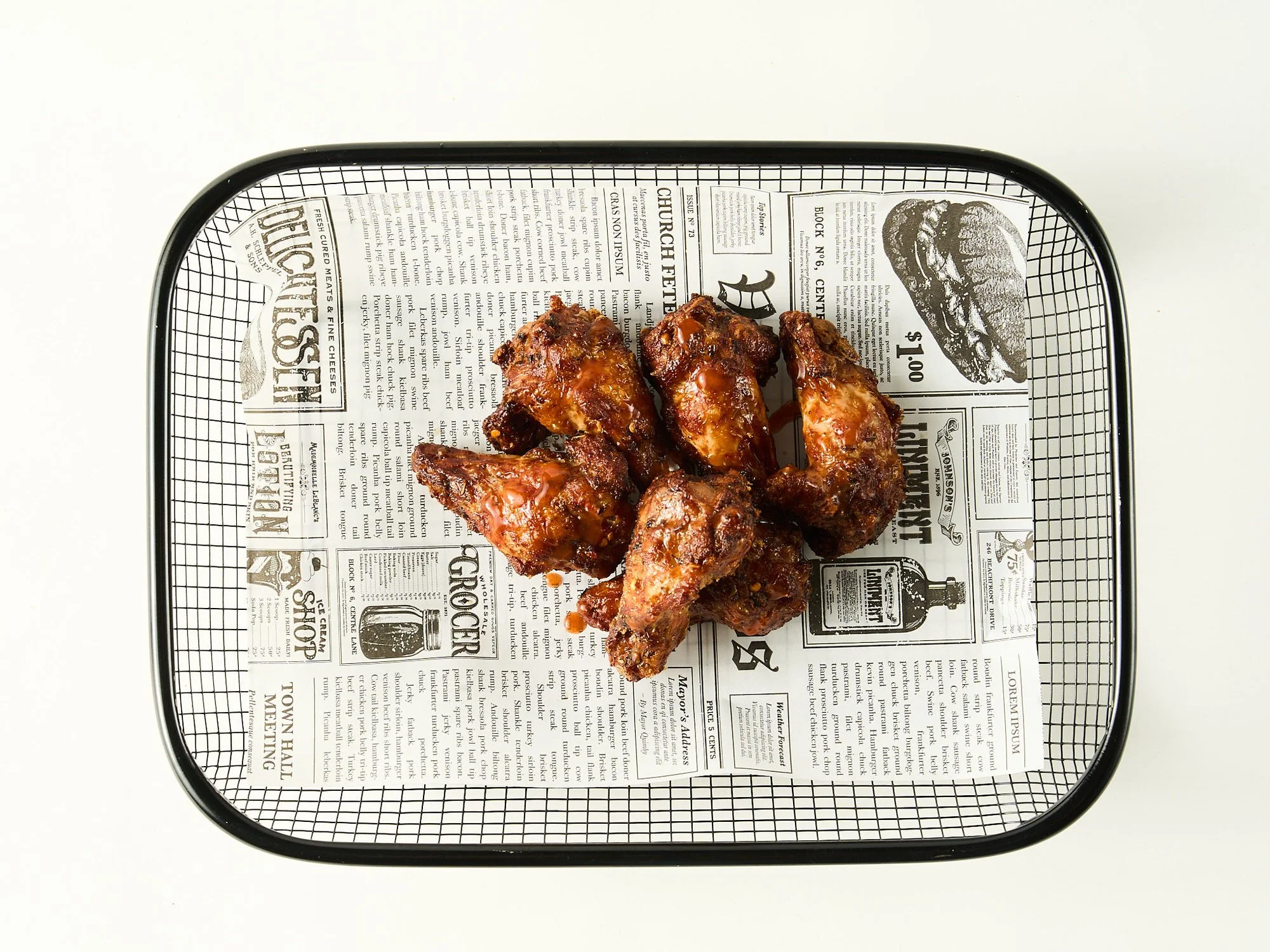 Noen bortskjæret kyllingvinger med BBQ-saus på en svart metallbrett med avisdesign.