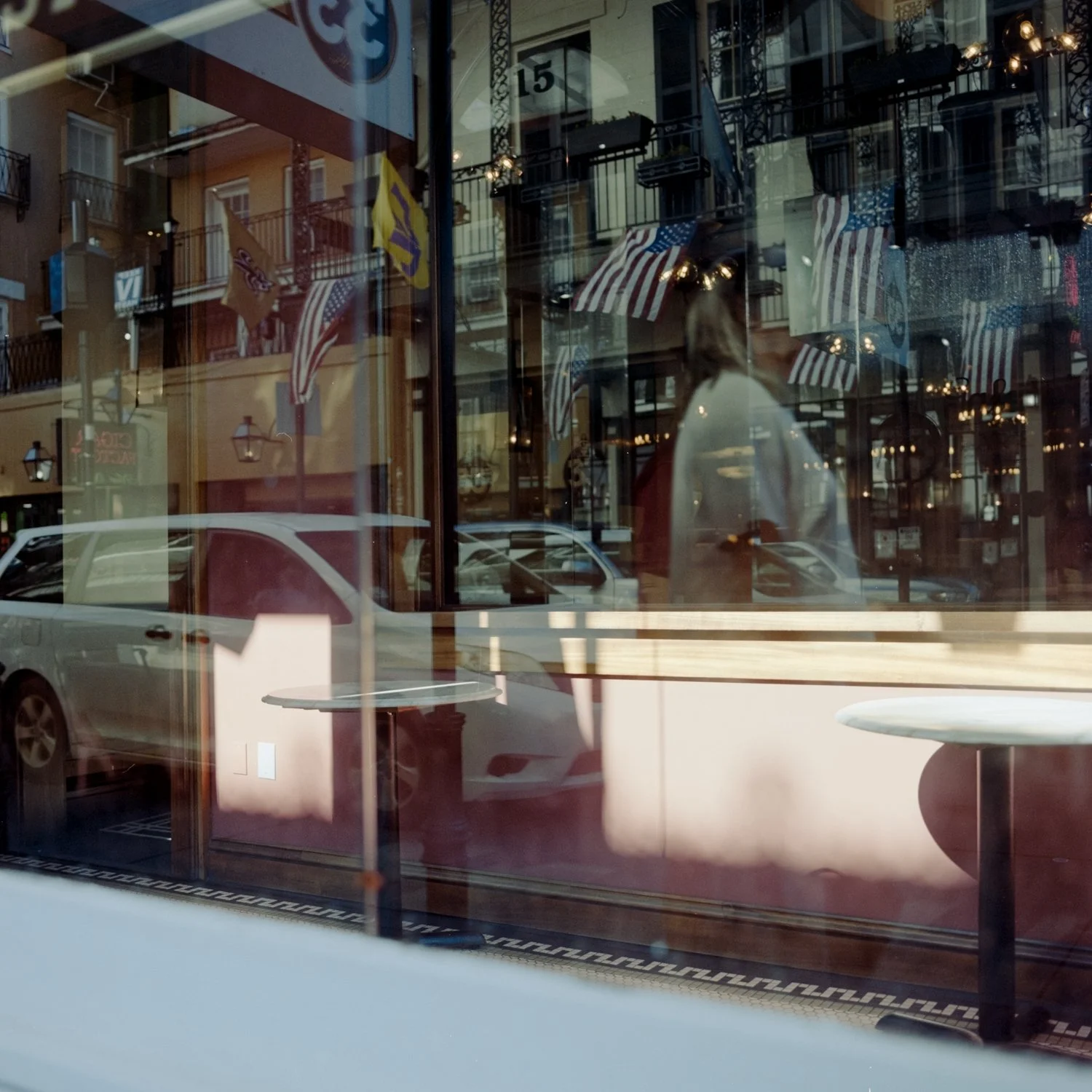 Reflection of buildings, flags, cars, and a person on a glass window of a shop or cafe.