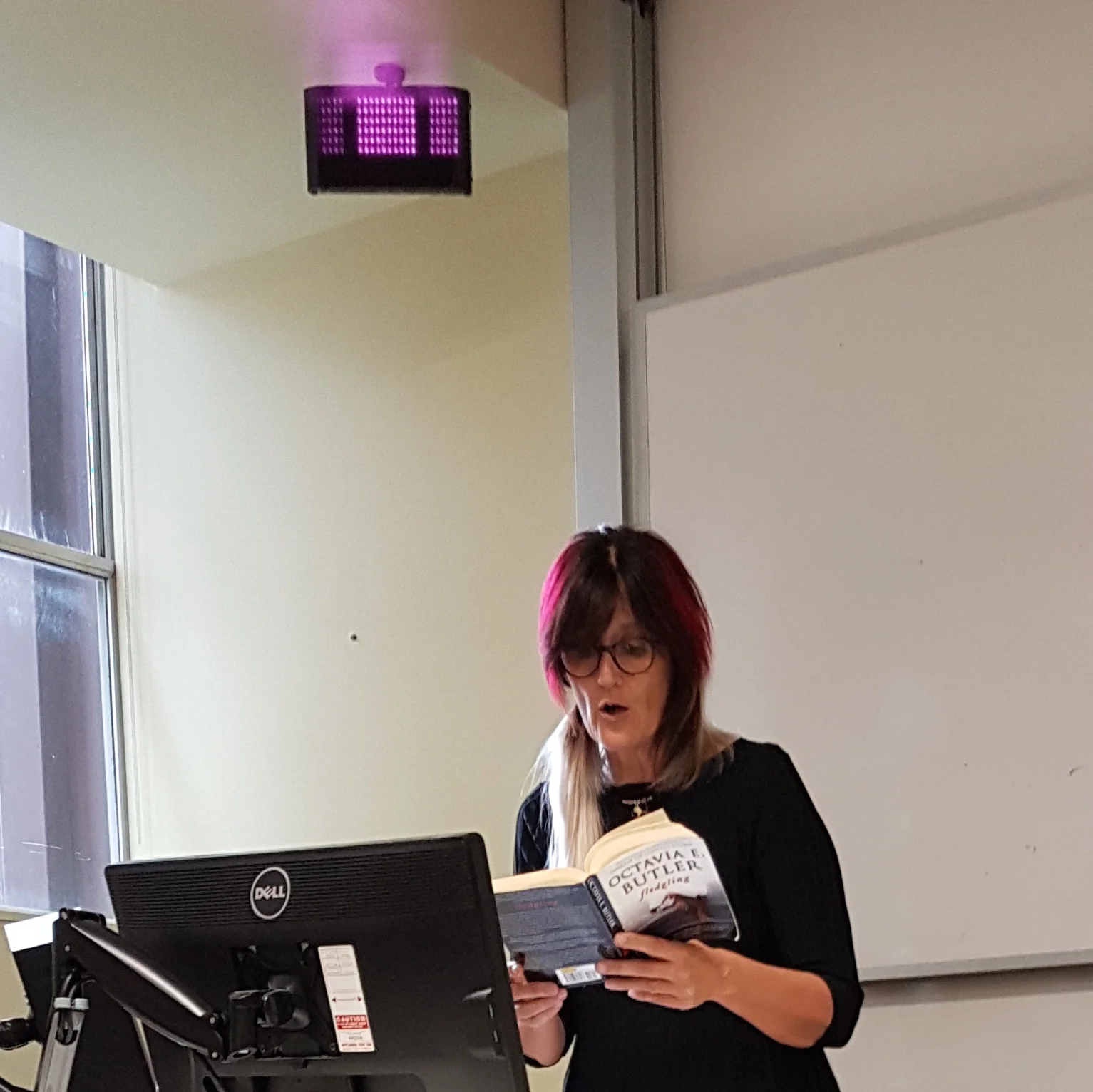 Speculative fiction author Marianne de Pierres giving a lecture on Octavia Butler's Fledgling , with a poltergeist overhead.