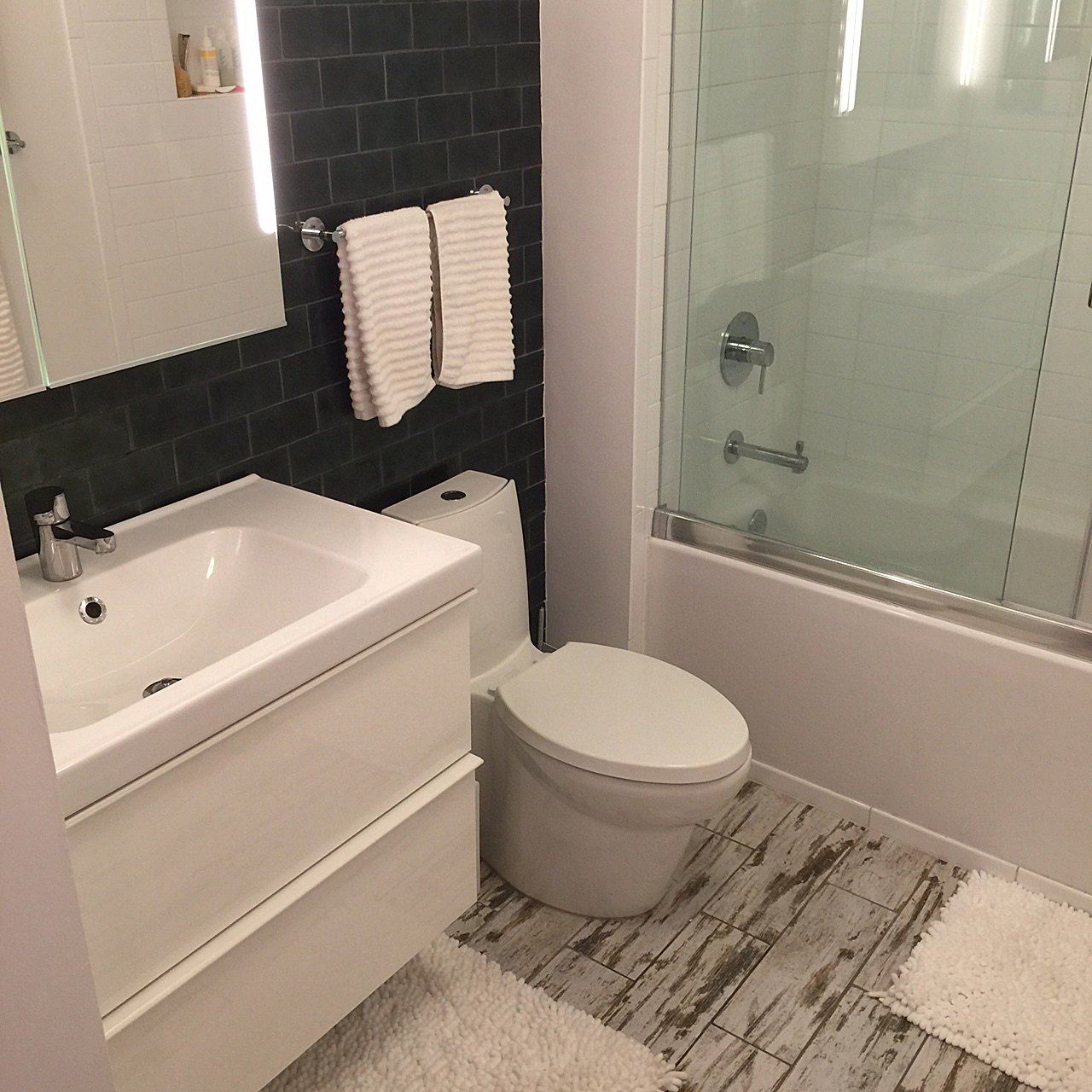 A new wall-mounted vanity, tile, lighting, and plumbing fixtures modernize the bathroom