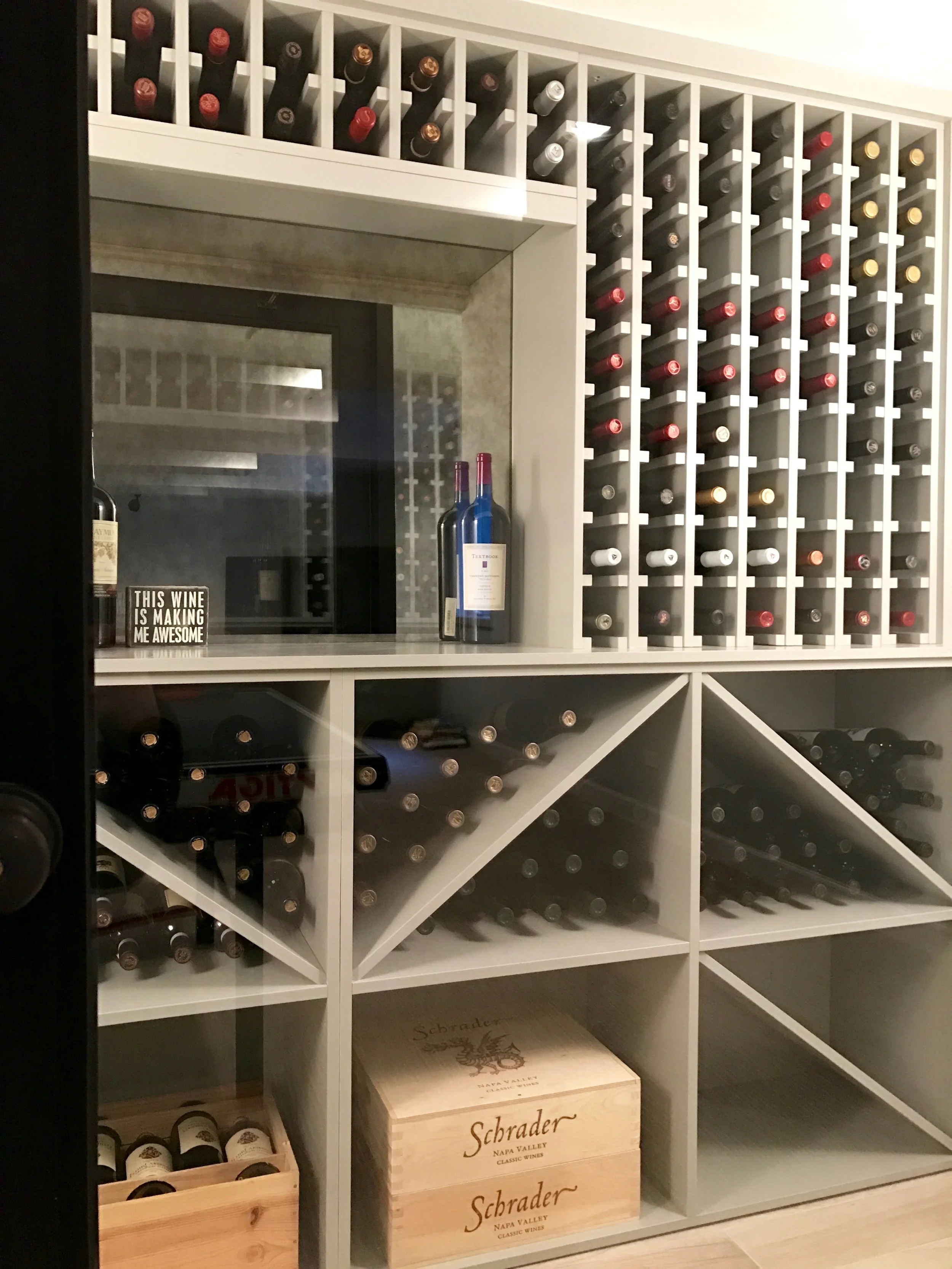 Another look at the wine storage with antiqued mirror glass in the center and multiple storage options to accommodate different wine formats. The custom wine storage unit is a modernized version on the traditional dark wood cabinetry commonly found in wine cellars. The bottom shelves are removable for case storage. 