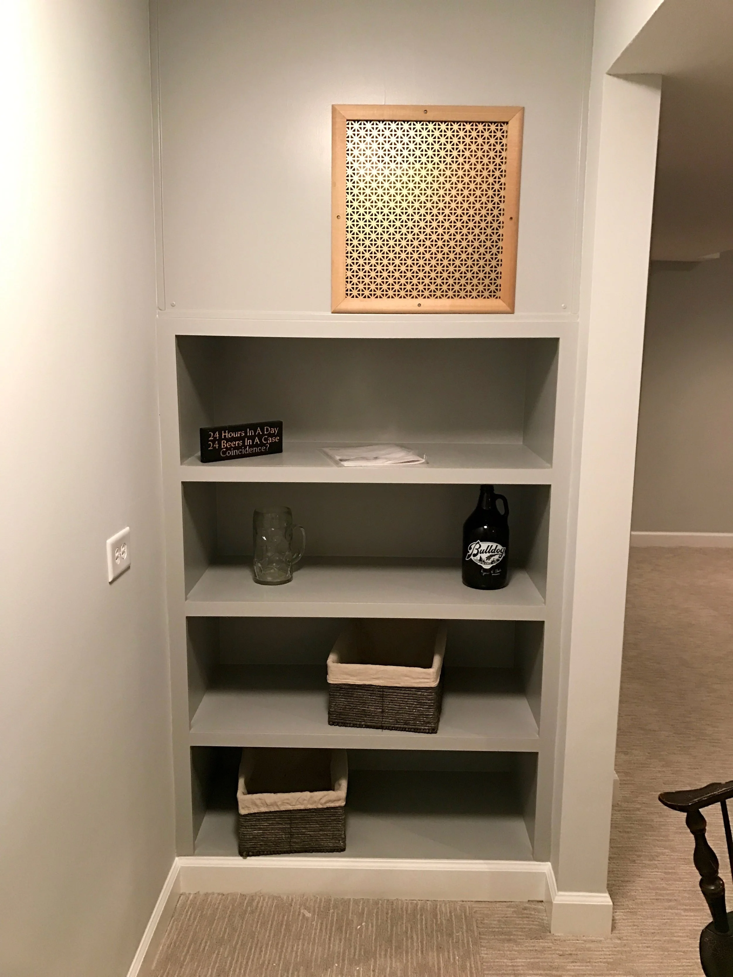 One design problem with wine cooling units is that they often project out of the wall much like a window-mounted air-conditioner. In this instance, we built a custom shelving unit with a grill to allow for additional storage, air transfer, and better visuals. Removable panels allow for easy access to the wine cooling unit if it needs service.