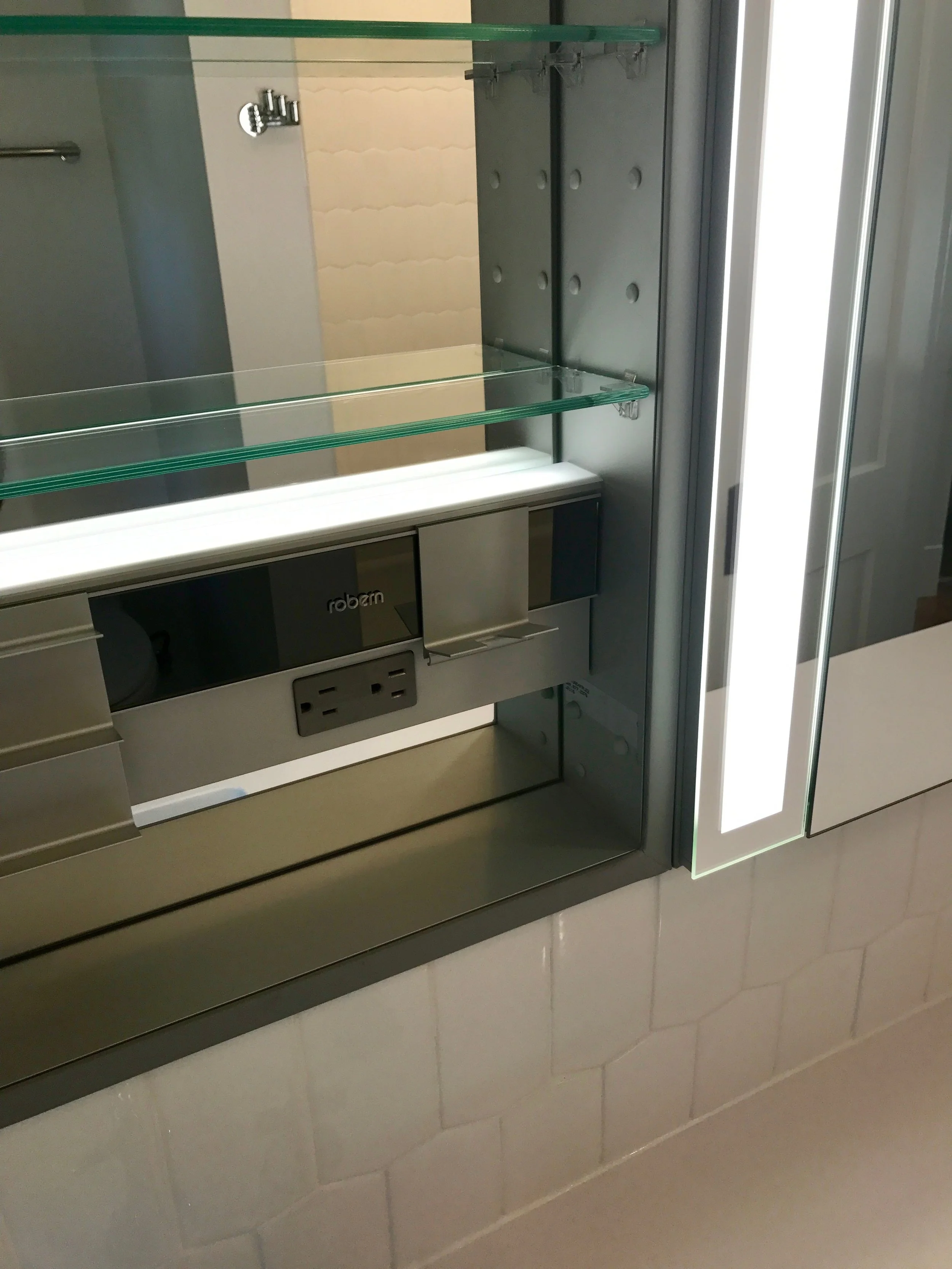 Three recessed medicine cabinets add useful above-sink storage for the owners. This version comes with integrated lighting, an electrical outlet, and built-in interior lighting to illuminate the inside of the cabinet. It even has a thingy to hang your razor or toothbrush. If you install it, you can call it a thingy. 
