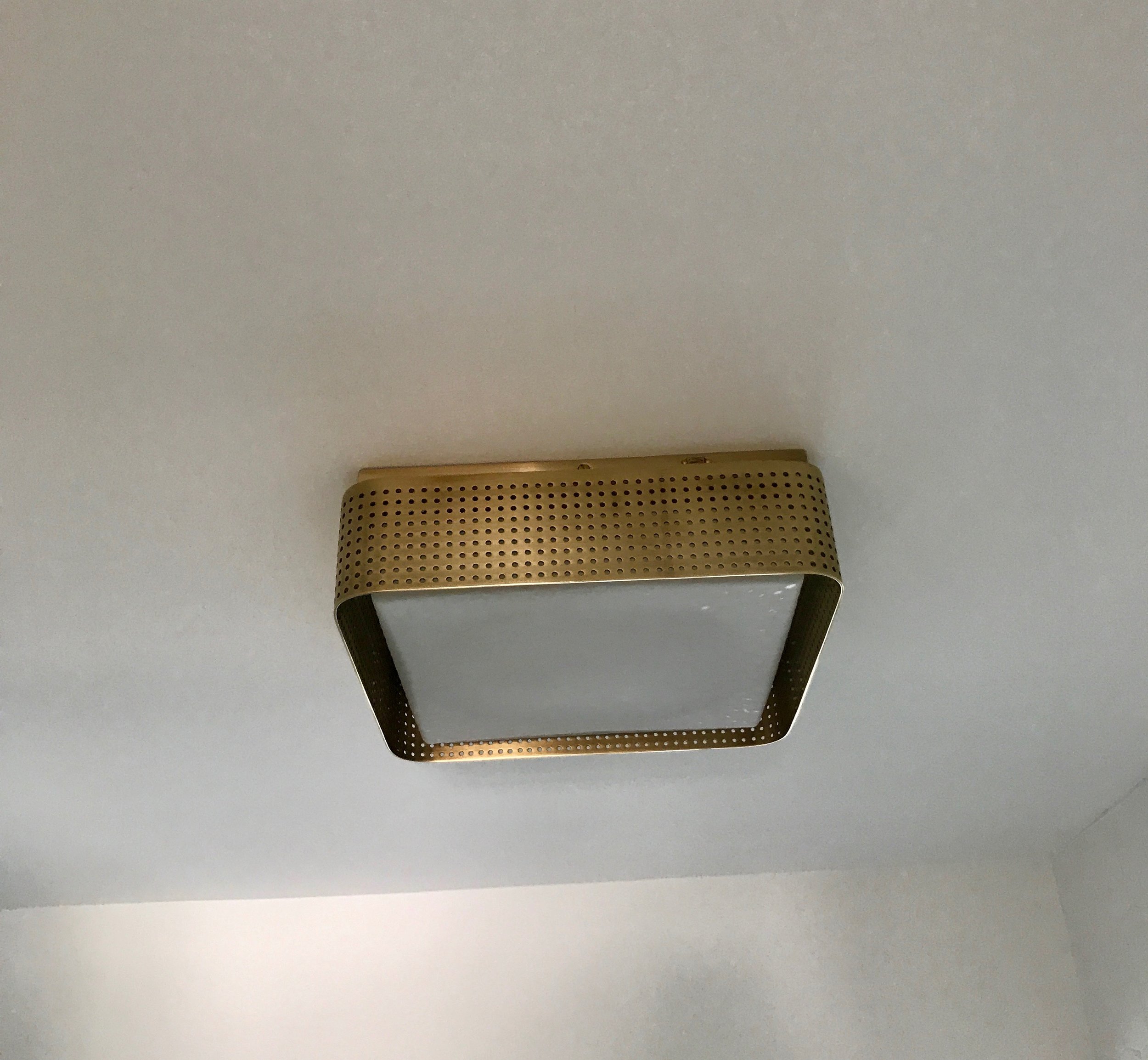 The Kelly Wearstler brass-wrapped ceiling light echoes the vanity pulls. 