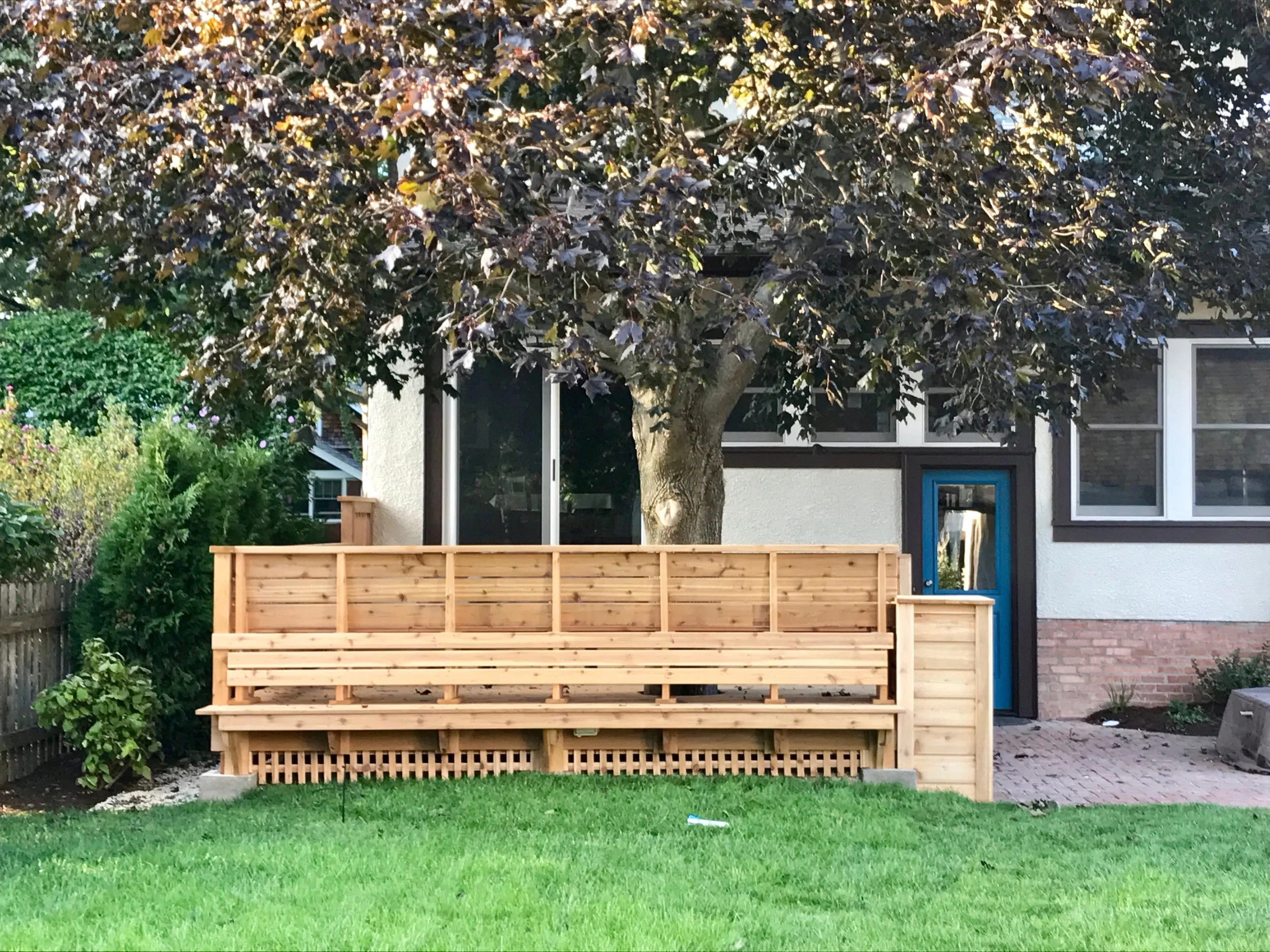 A view of the rear of the house and a second bench, this one facing the backyard. The large canopy of the maple tree provides ample shade.