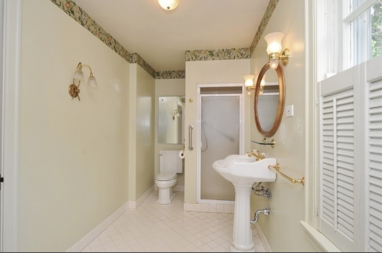 The original master bathroom featured a 36" x 36" shower, a green wallpaper border near the ceiling, and gold accents. An orphaned pedestal sink stood guard on the 14 foot long wall. 