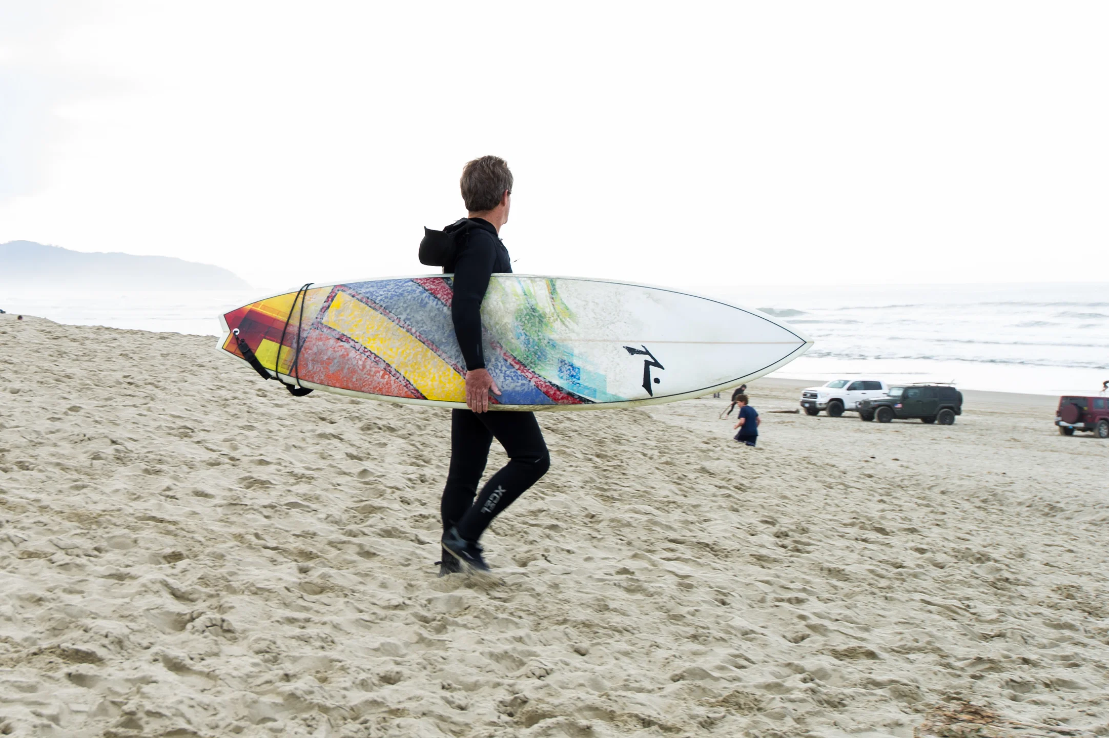 Surfer walks towards water along Oregon Coast at Cape Kiwanda