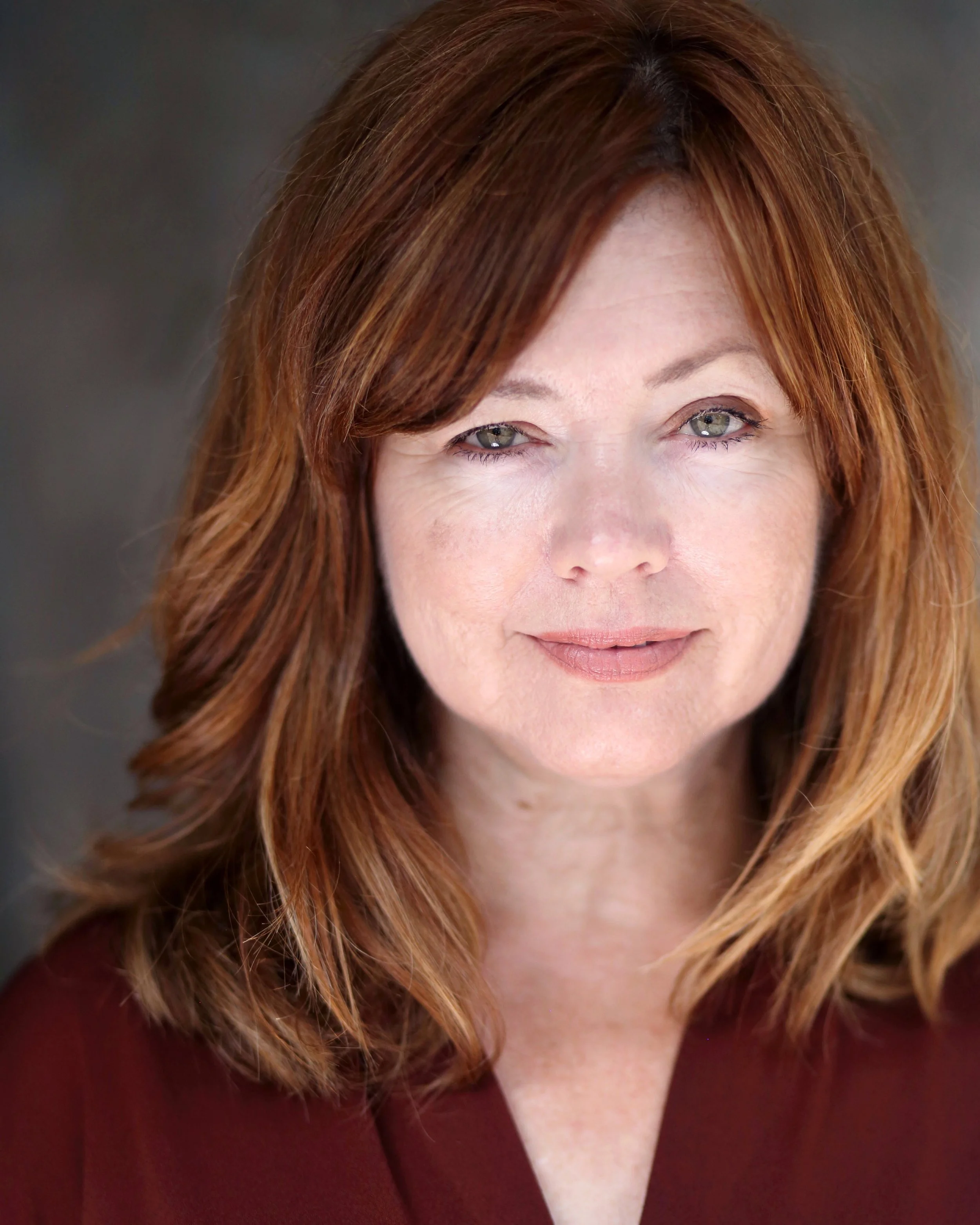 white woman 50's auburn hair slight curl shoulder length green eyes slight smile looking at camera, rust colored shirt
