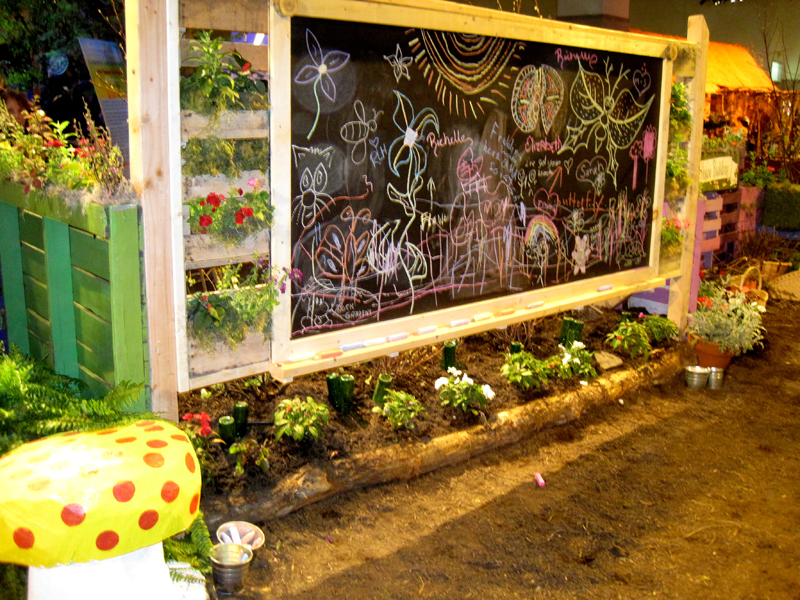 A chalkboard is surrounded by vertical gardens made of palettes.