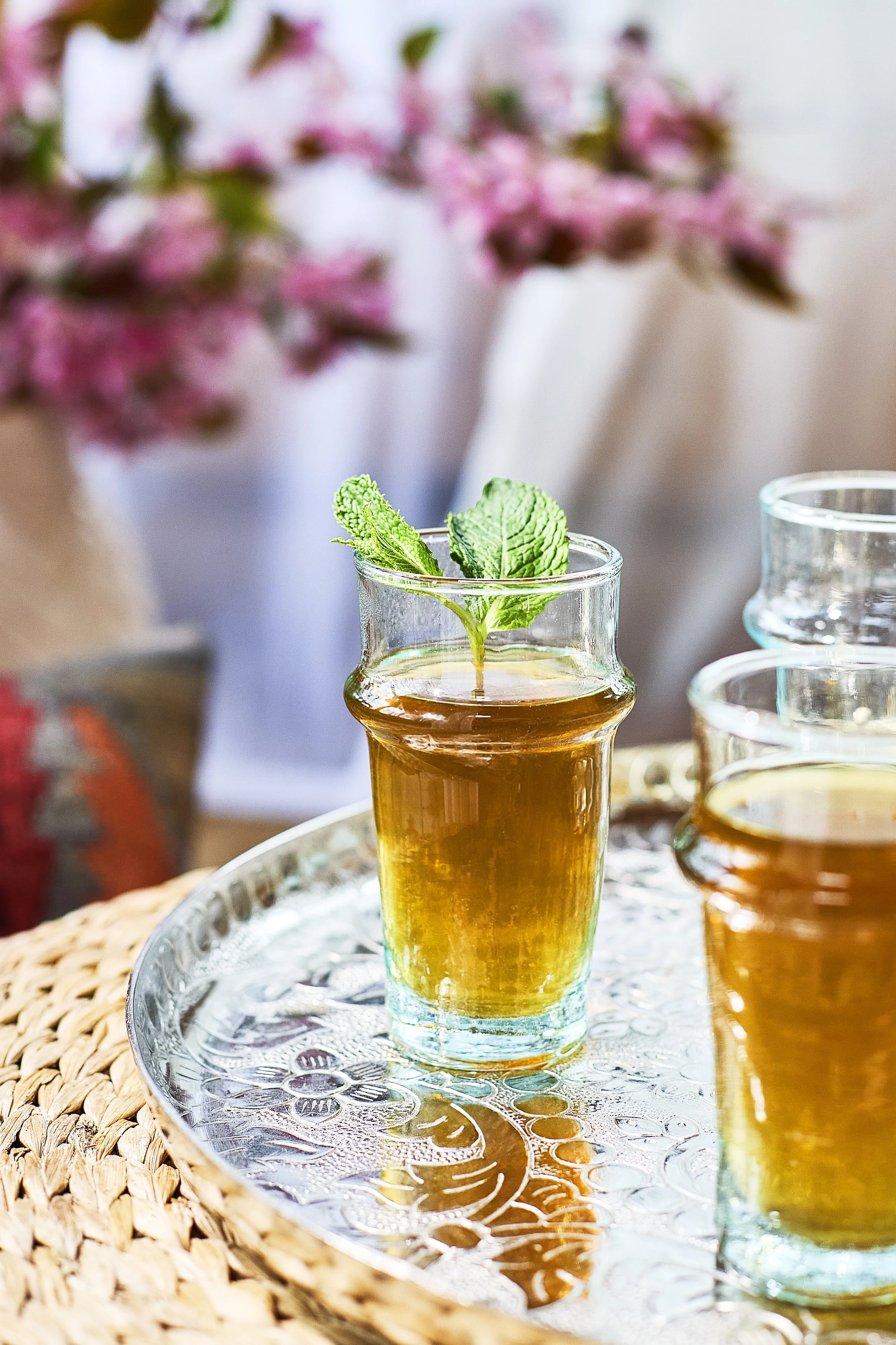 Close-up of a glass with a mint sprig, filled with a golden beverage, placed on a decorative silver tray.