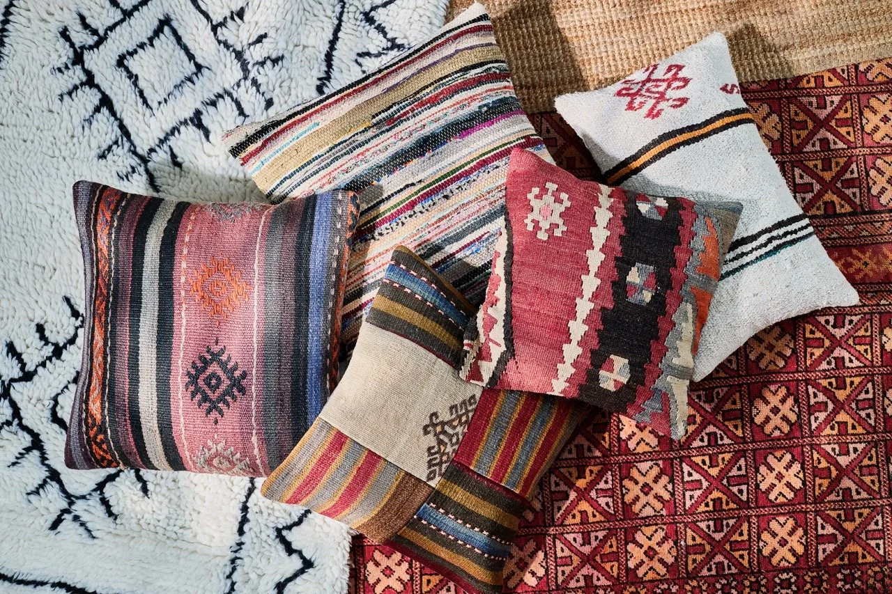 A collection of colorful, patterned decorative pillows placed on a textured area rug with a geometric design.