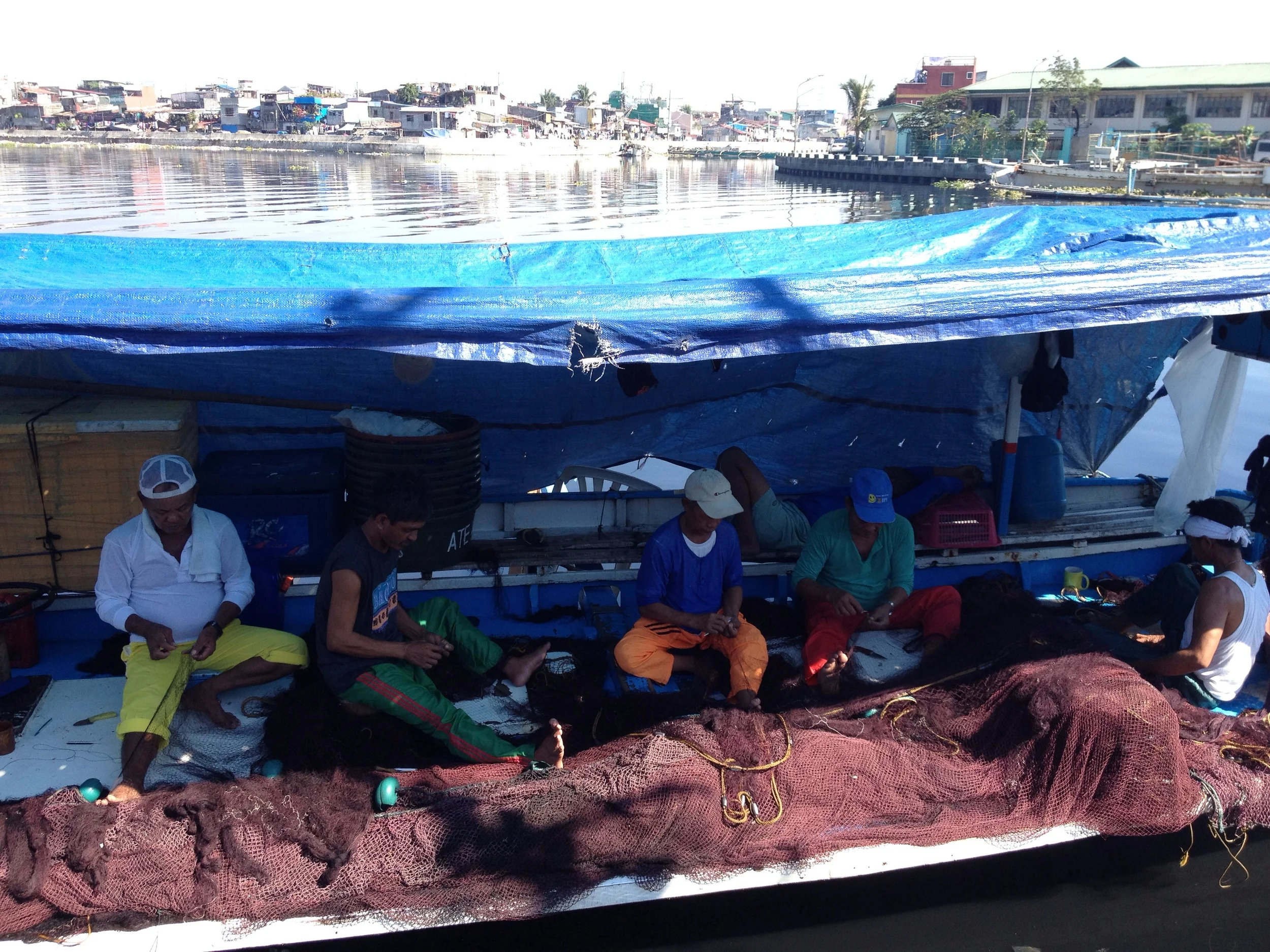 Fishermen repair nets on a hot afternoon along the Navotas River. 