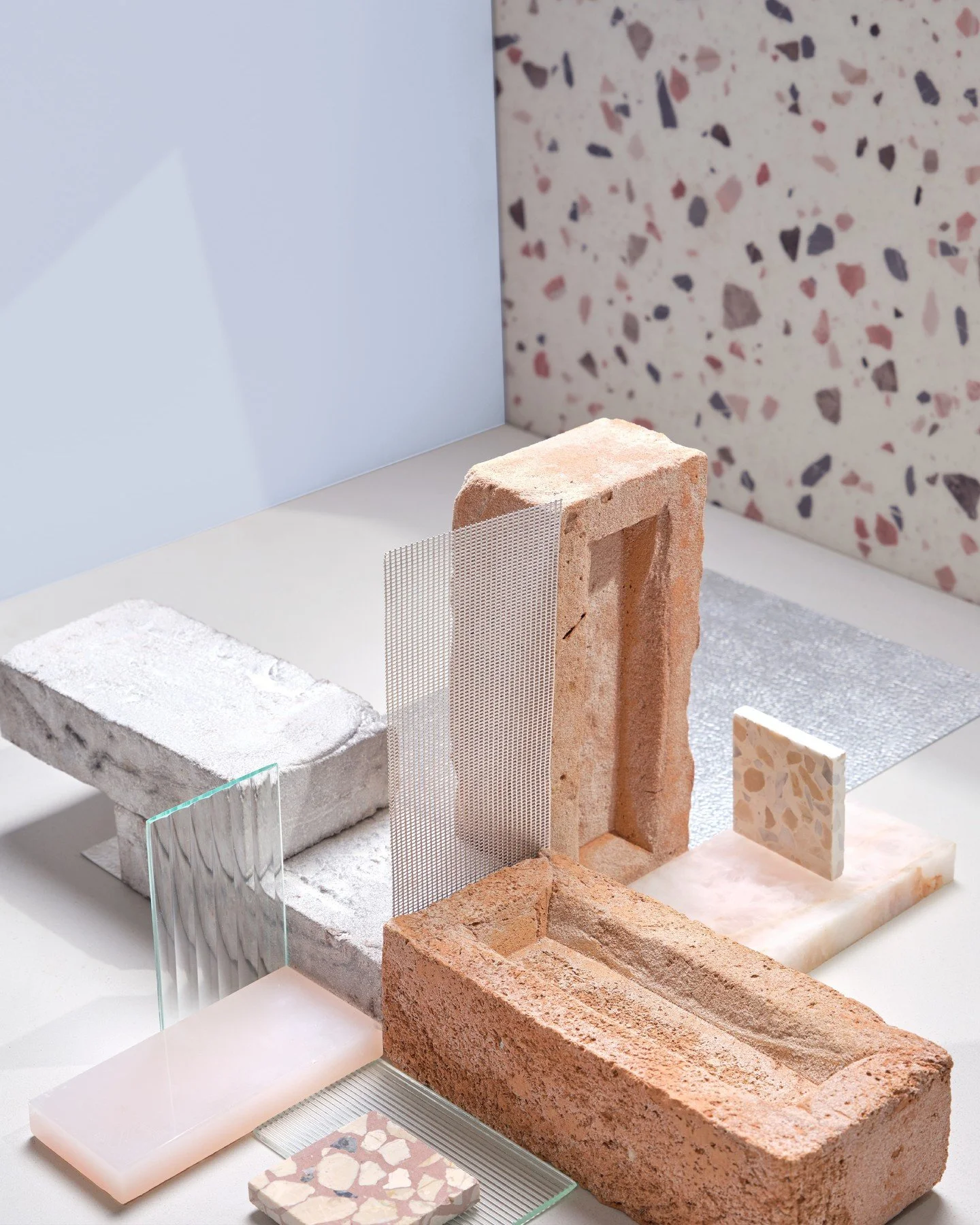 A refined composition where industrial textures meet playful sophistication. This mood board brings together rough brick, pale concrete, terrazzo, rippled and frosted glass, polished stone, and fine metal mesh. Soft pastel tones contrast beautifully