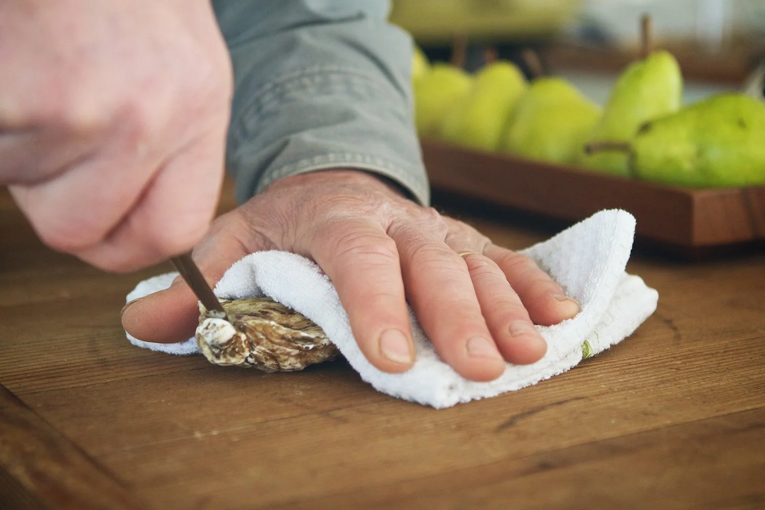 Hold the oyster firmly under the towel on a cutting board or table top, cup side down. Wiggle your knife between the two shells at the tip of the oyster as shown in the picture.