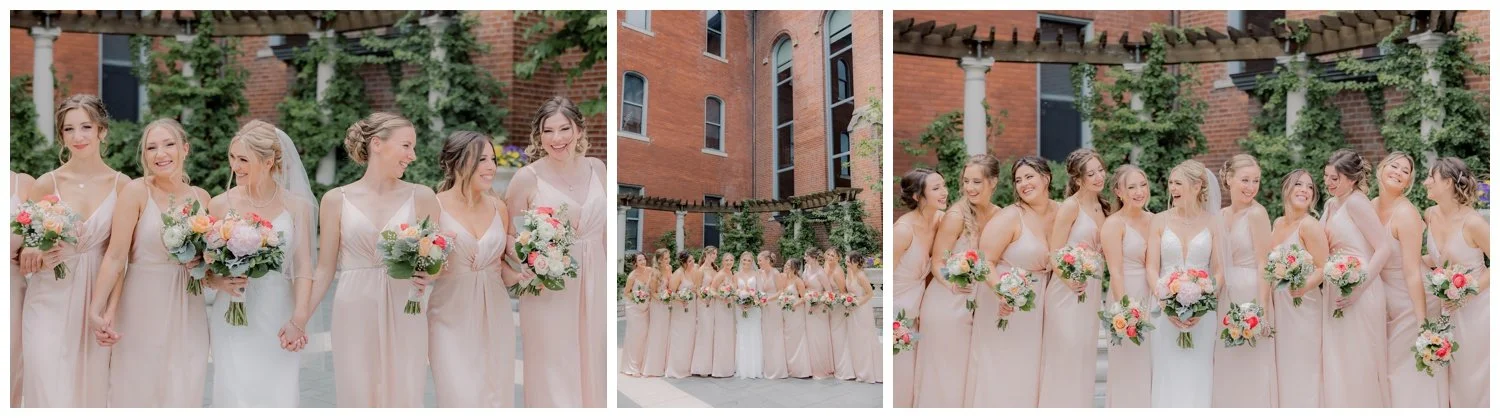 A bride and her many bridesmaids in blush pink gowns and bright pink, yellow, peach, and orange flowers.