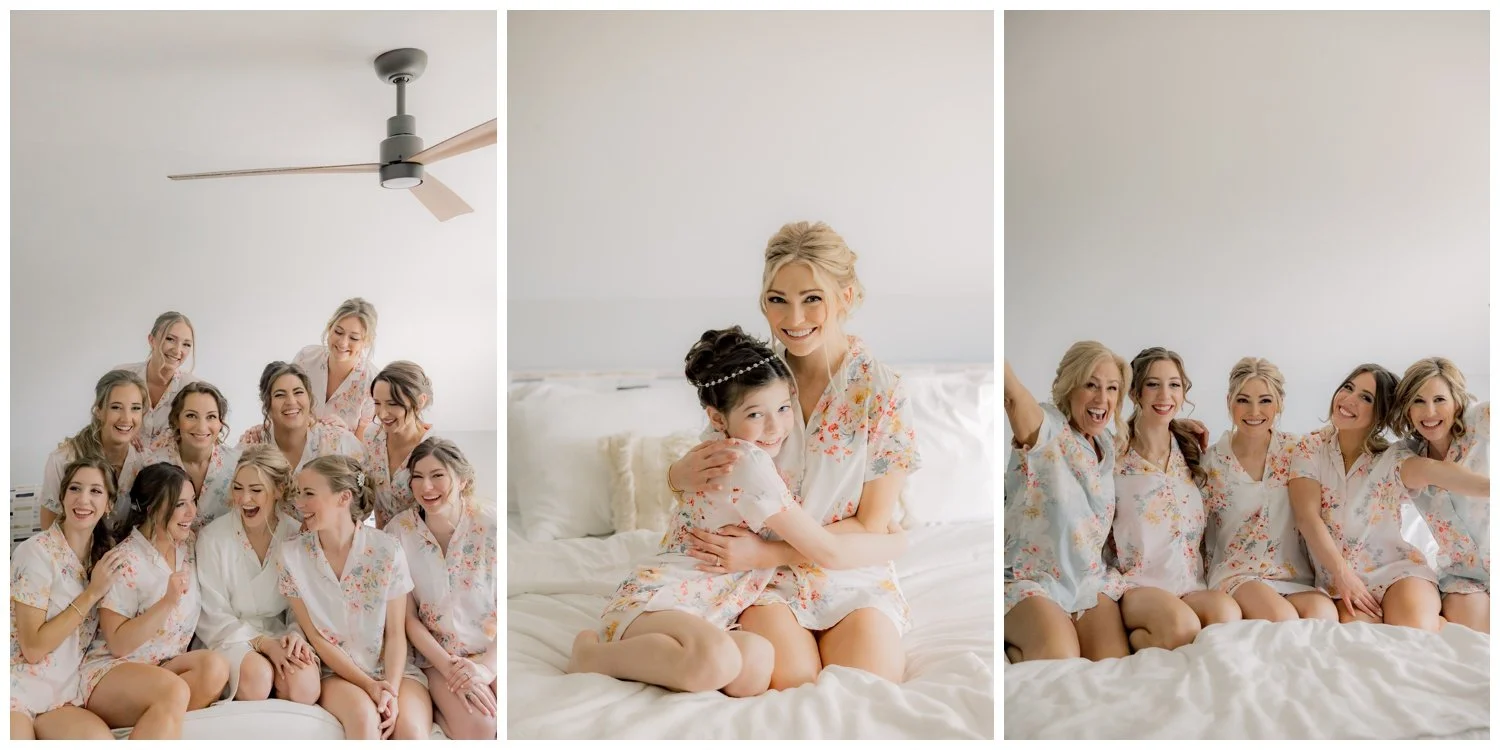A bride and her bridesmaids smiling the morning of her wedding day on a bed in matching pajamas.