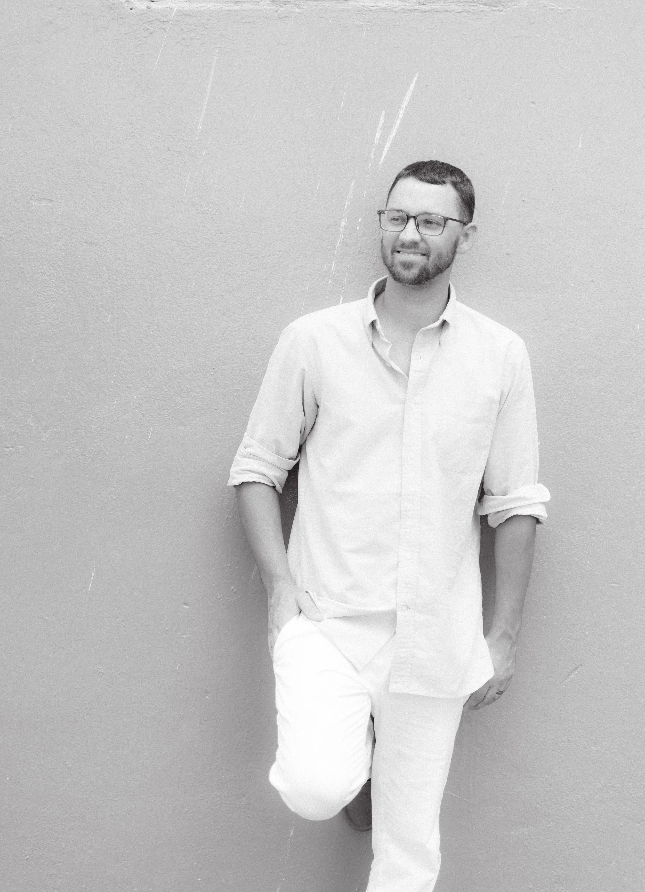 Black and white images of kris wearing all white leaning against wall.