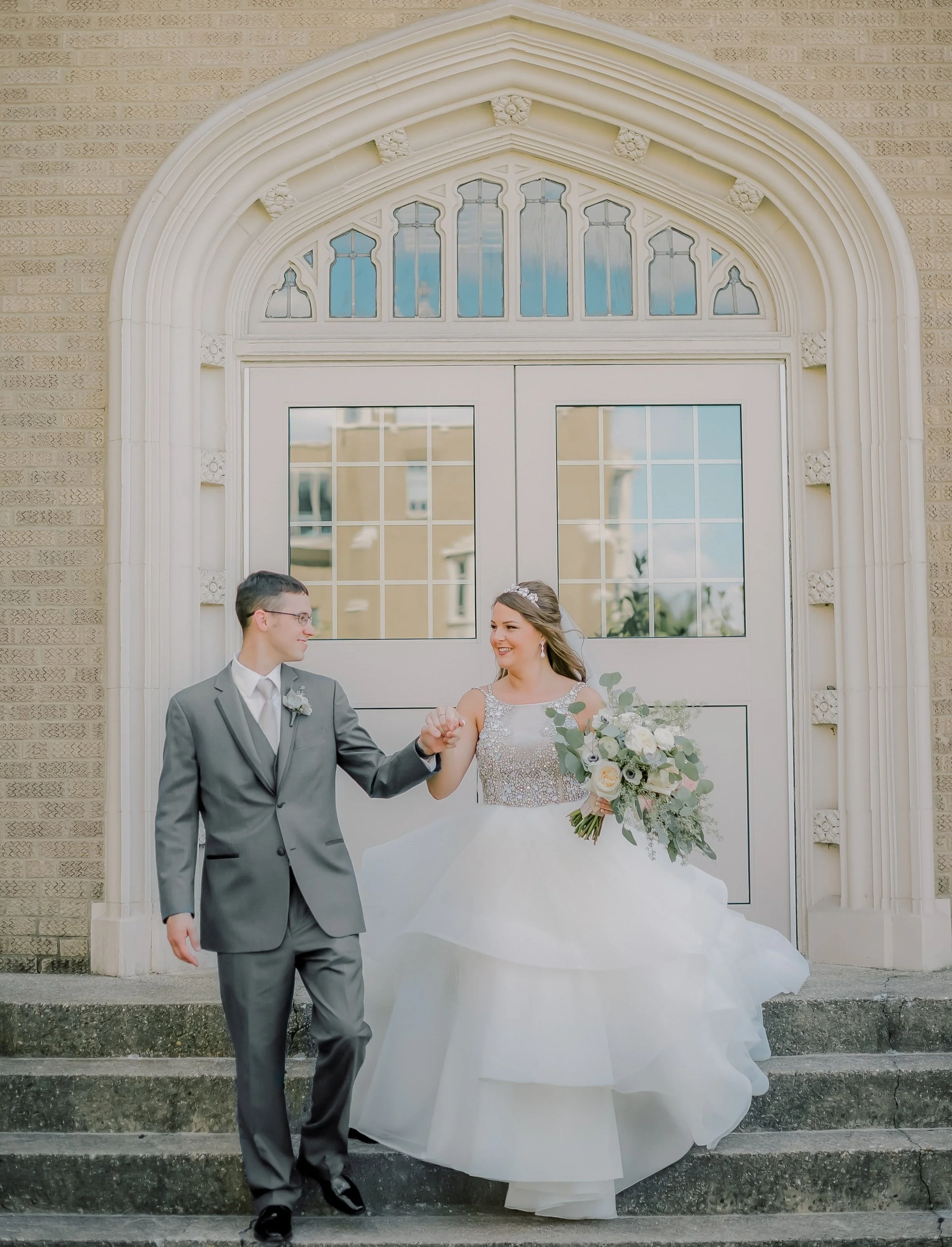 Abbie and Kris on their wedding day walking down a staircase at Xavier University while Abbie wears a Hayley Paige wedding gown.