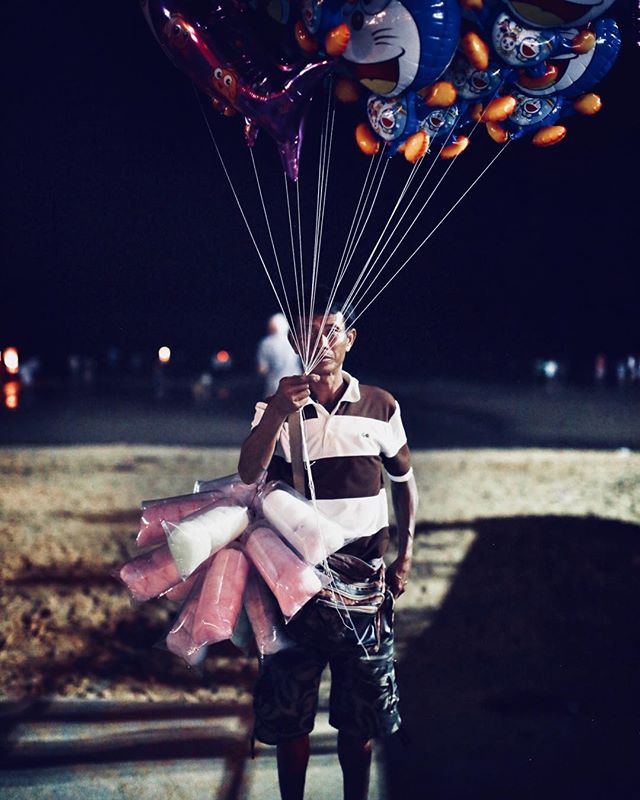 There is something interesting to me about this photo. He seems to be hiding behind his balloons. He also is looking directly at me. 
I originally was disappointed about the man In white behind his head but it it does bring him out of the background 