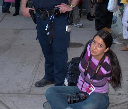 NYPD-credentialed photojournalist Julia Xanthos, wearing a 2007 NYPD-issued press credential along with a camera, under arrest by the NYPD for doing her job.