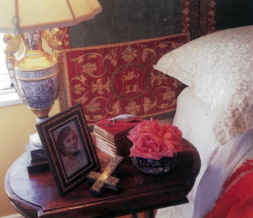 Bedside table with pink roses, a framed photograph and red patterned upholstery