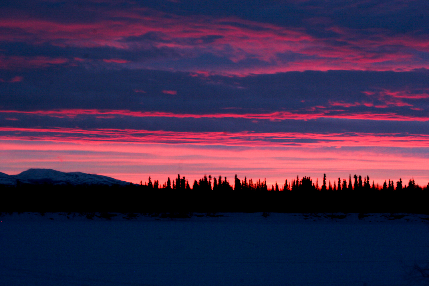   Sunrises are short and beautiful in Kobuk Valley National Park, enclosed by the Baird and Waring mountains. Inuchuck, 'Old Man Mountain' lies in the distance. The river, now frozen, is a source of life and sustenance for the villagers of Ambler who