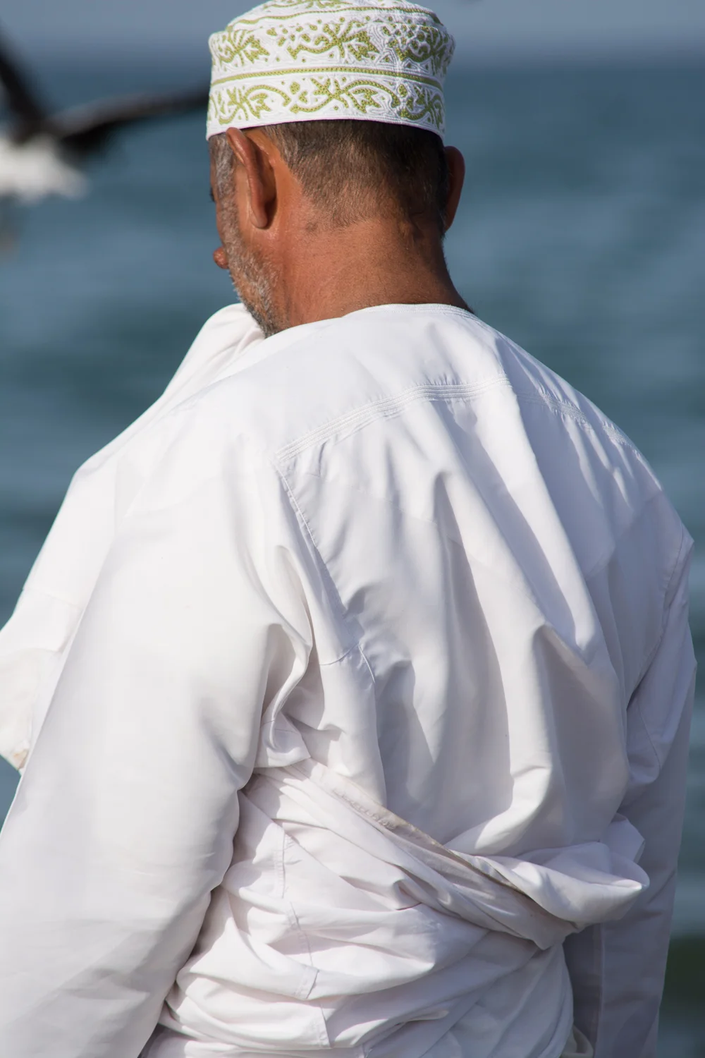 An Omani man holding the outer layer of his dish dash up to keep it dry.