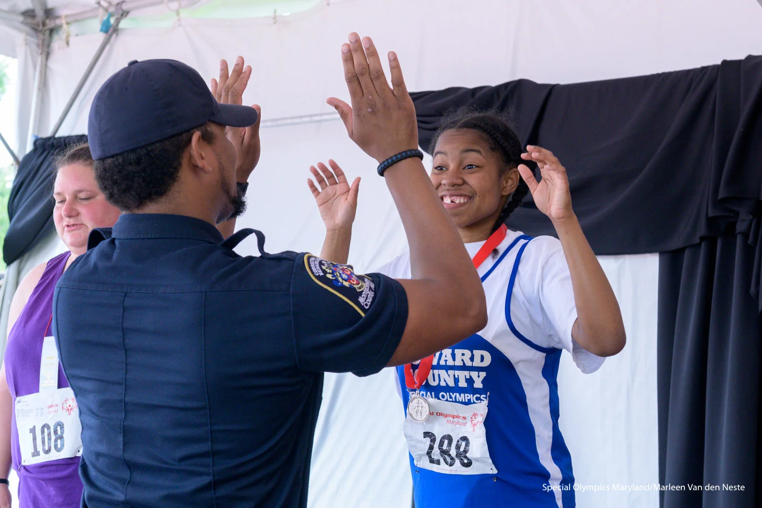 Athlete high-fiving a law enforcement officer after receiving a silver medal from him in the Awards tent at Unitas Stadium, Towson University, MD. on Sunday, June 9, 2019.