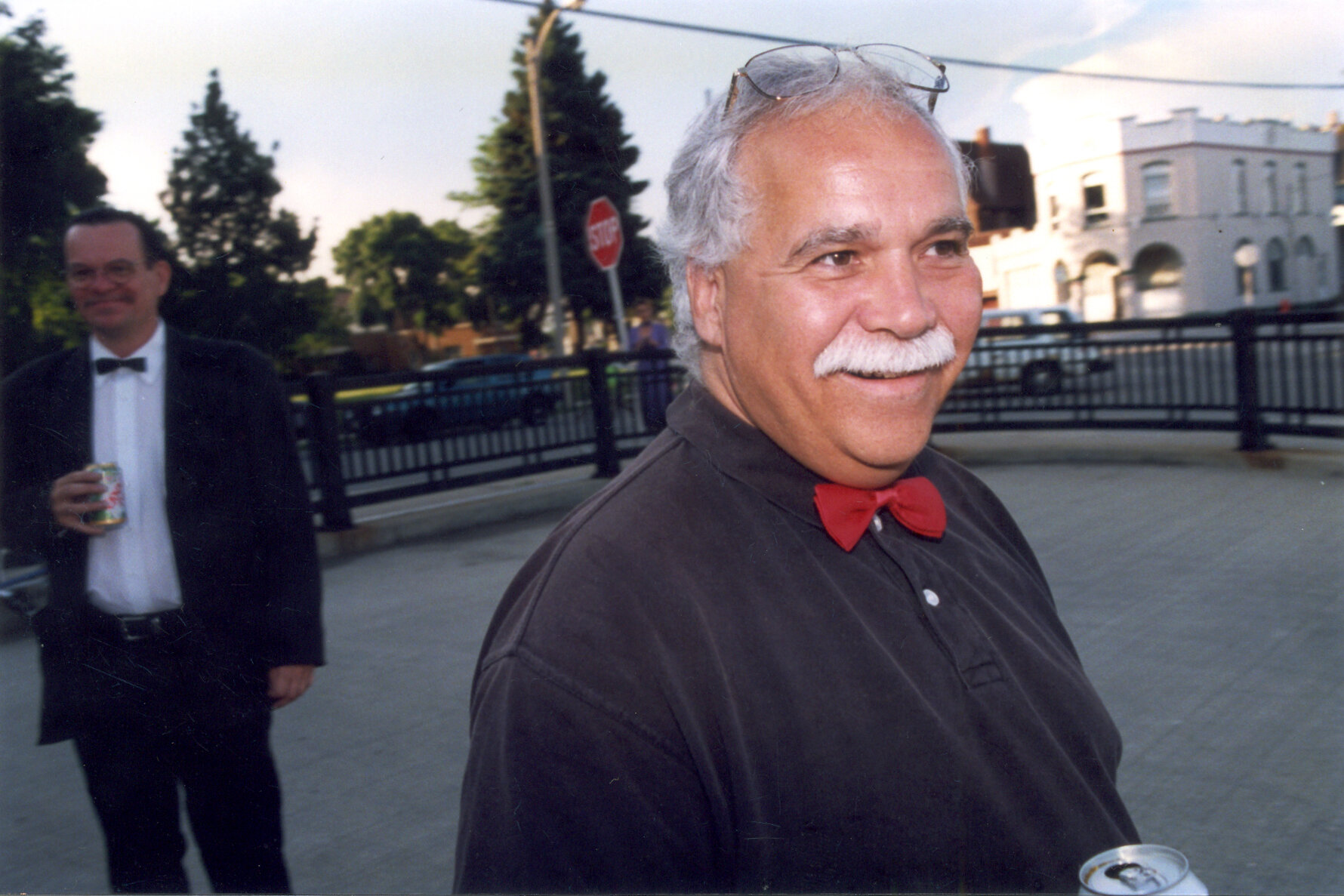 Man in black polo with red bow tie with glasses pushed on forehead smiles looking behind camera.