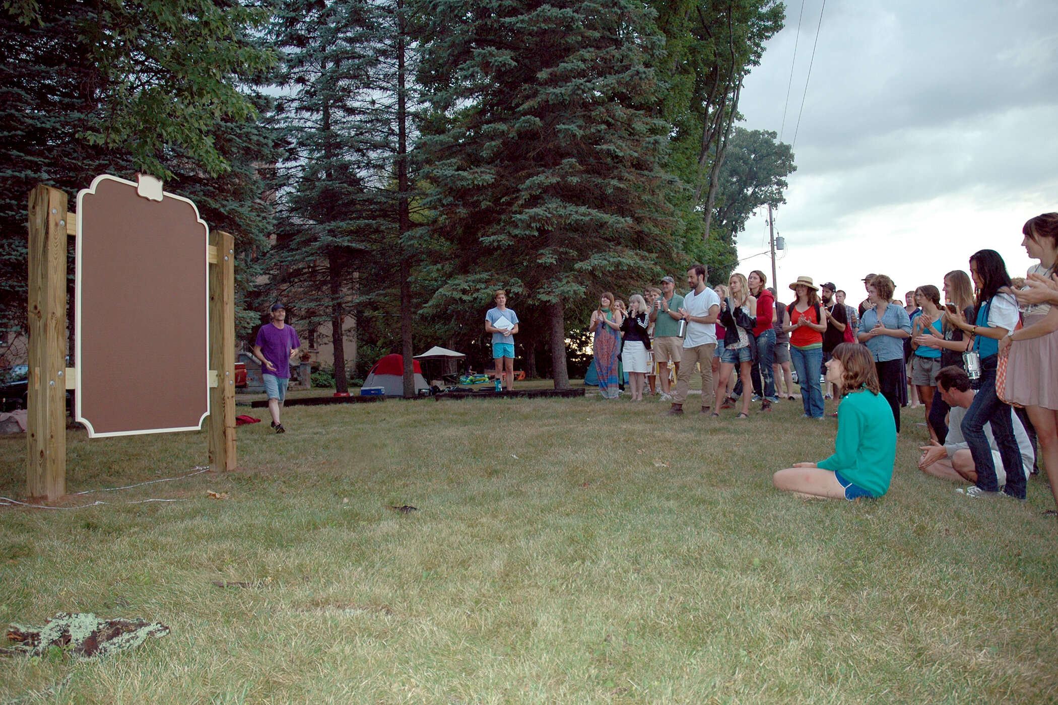 Man stands back, plaque fully uncovered, crowd gathered in front of plaque to view.