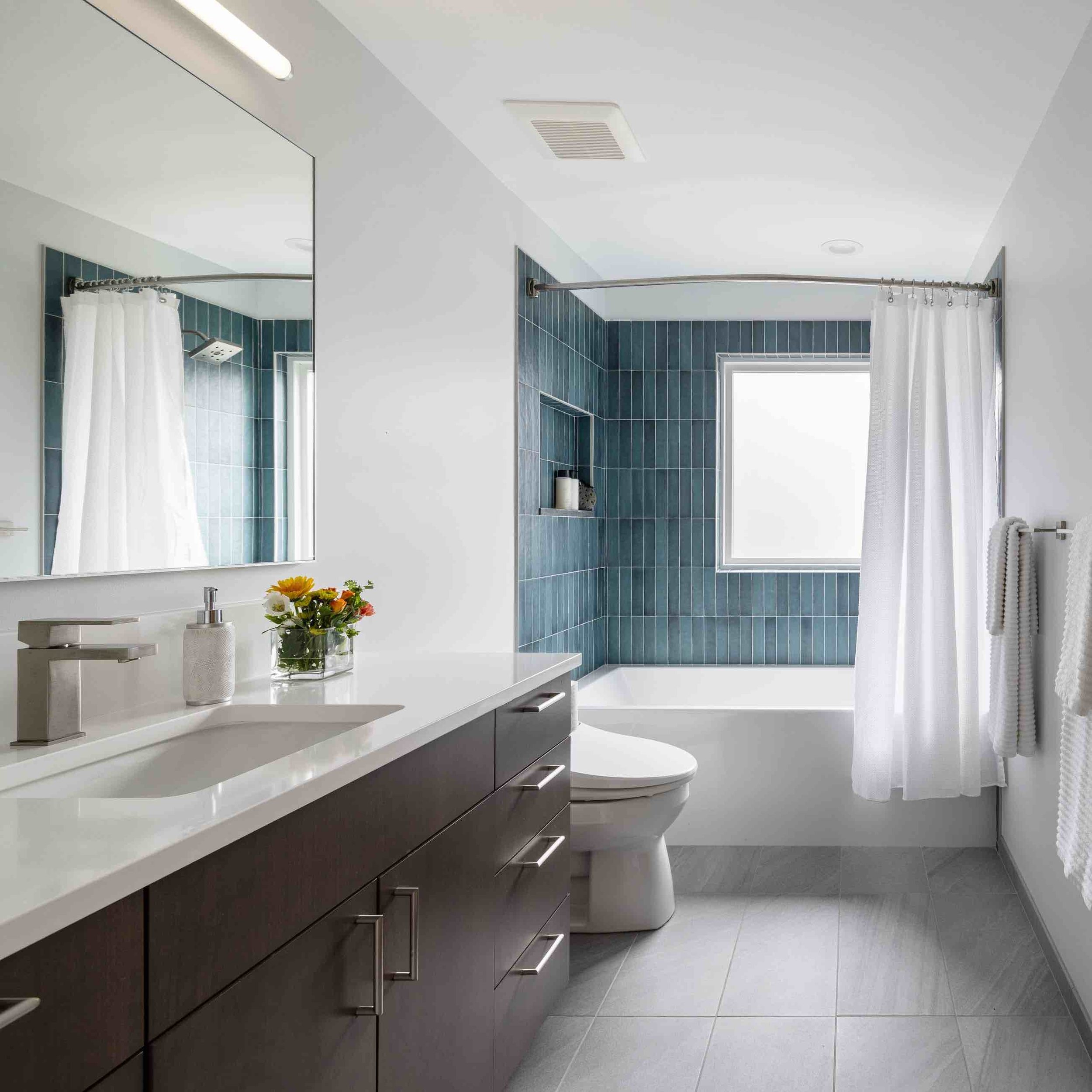 Double vaniety with dark wood cabinetry, white countertops, and blue tiled shower