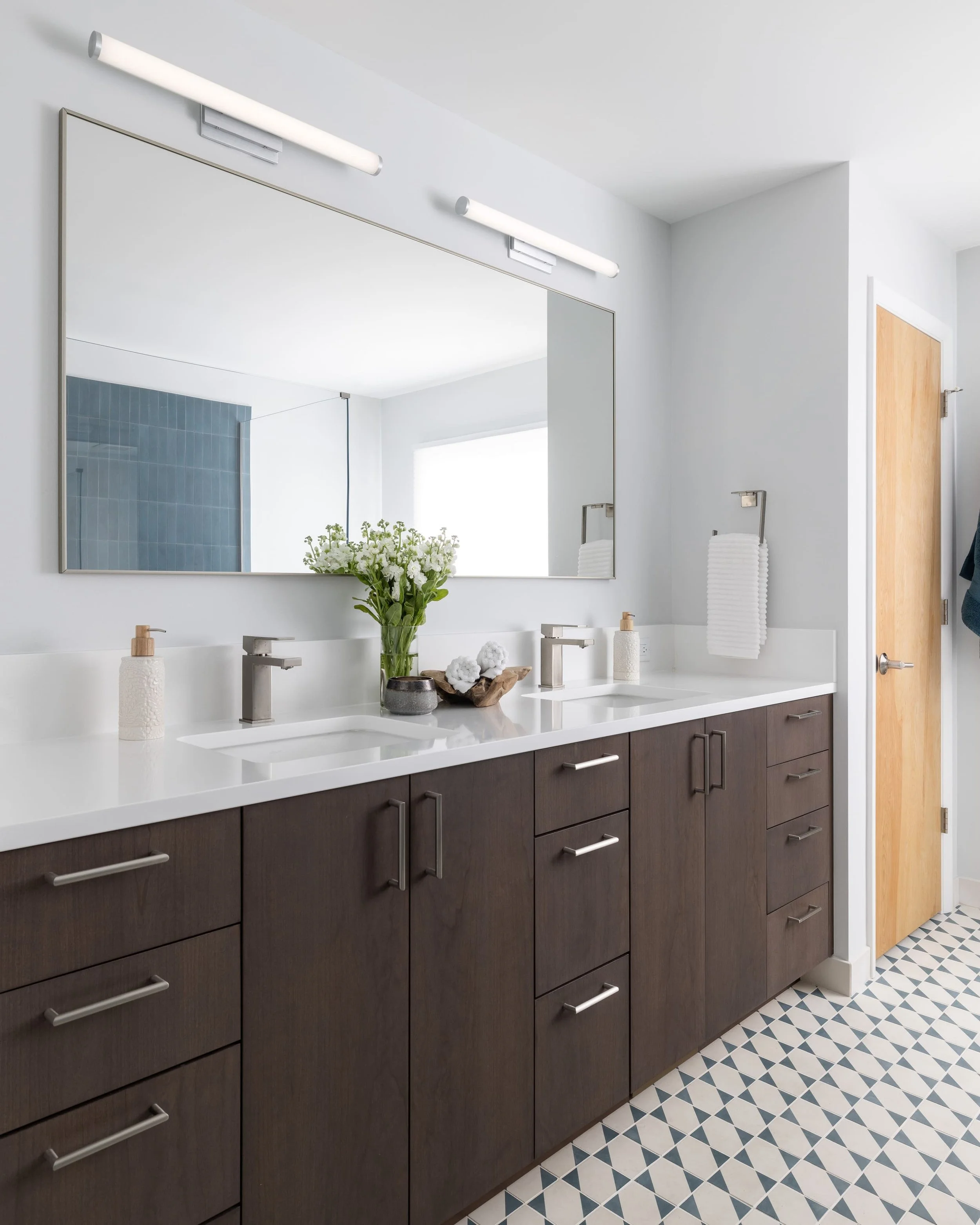 White countertops and dark wood cabinetry on double vanity in bathroom with black and white tiled floors
