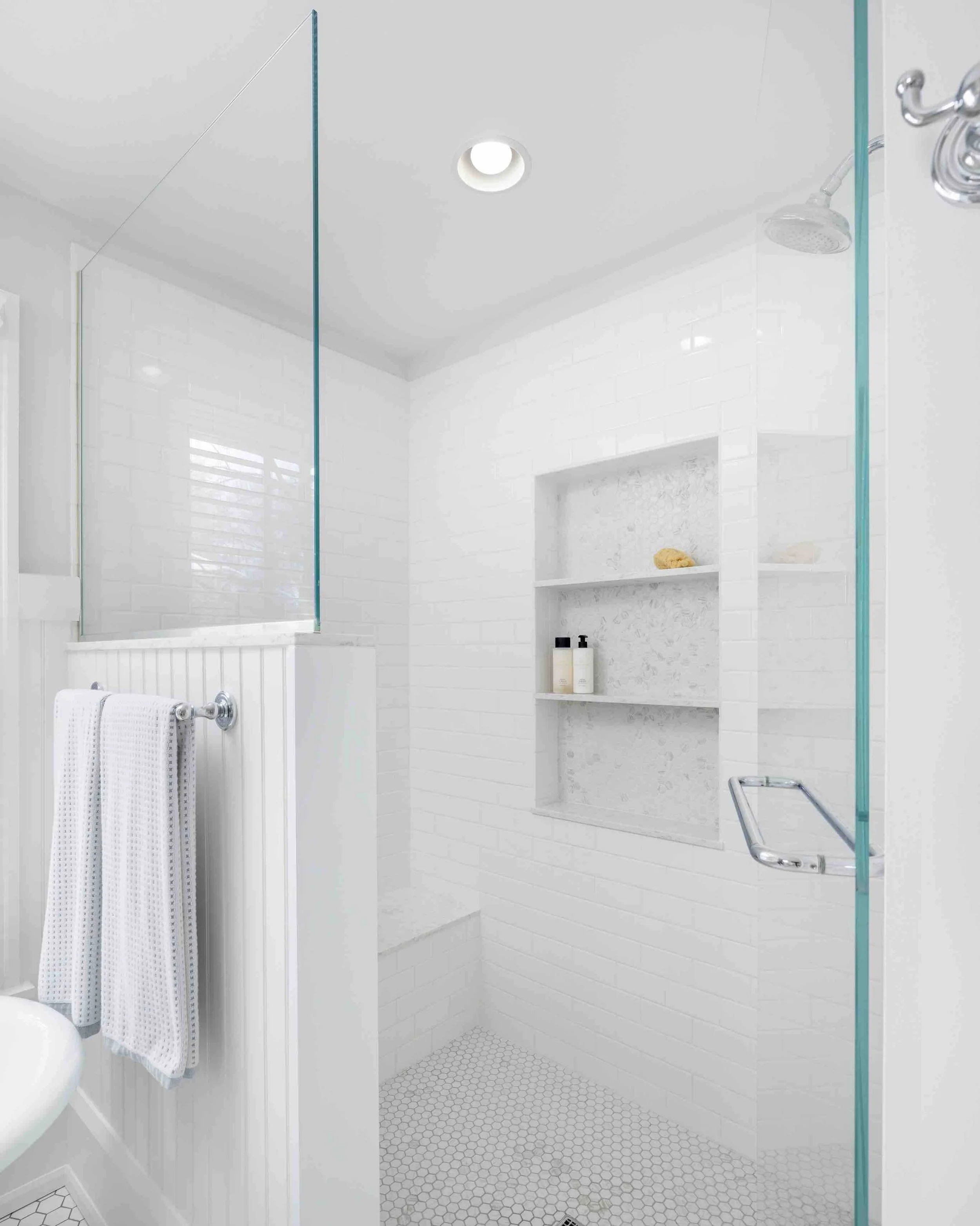 Custom white tiled shower with shower niche and glass door