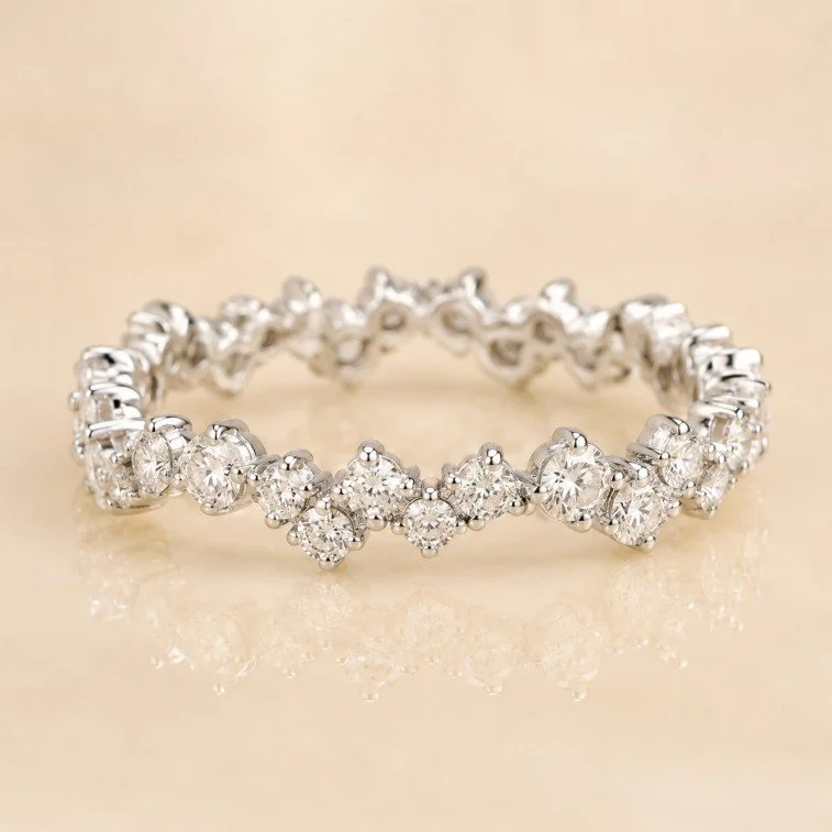 A silver diamond ring with multiple sparkling diamonds set in a circle, placed on a reflective light-colored surface.