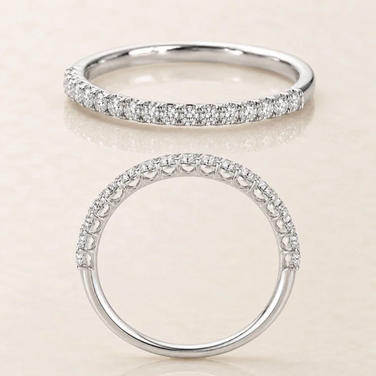 Two eternity-style rings with embedded gemstones, one lying flat and the other upright, on a light-colored surface.
