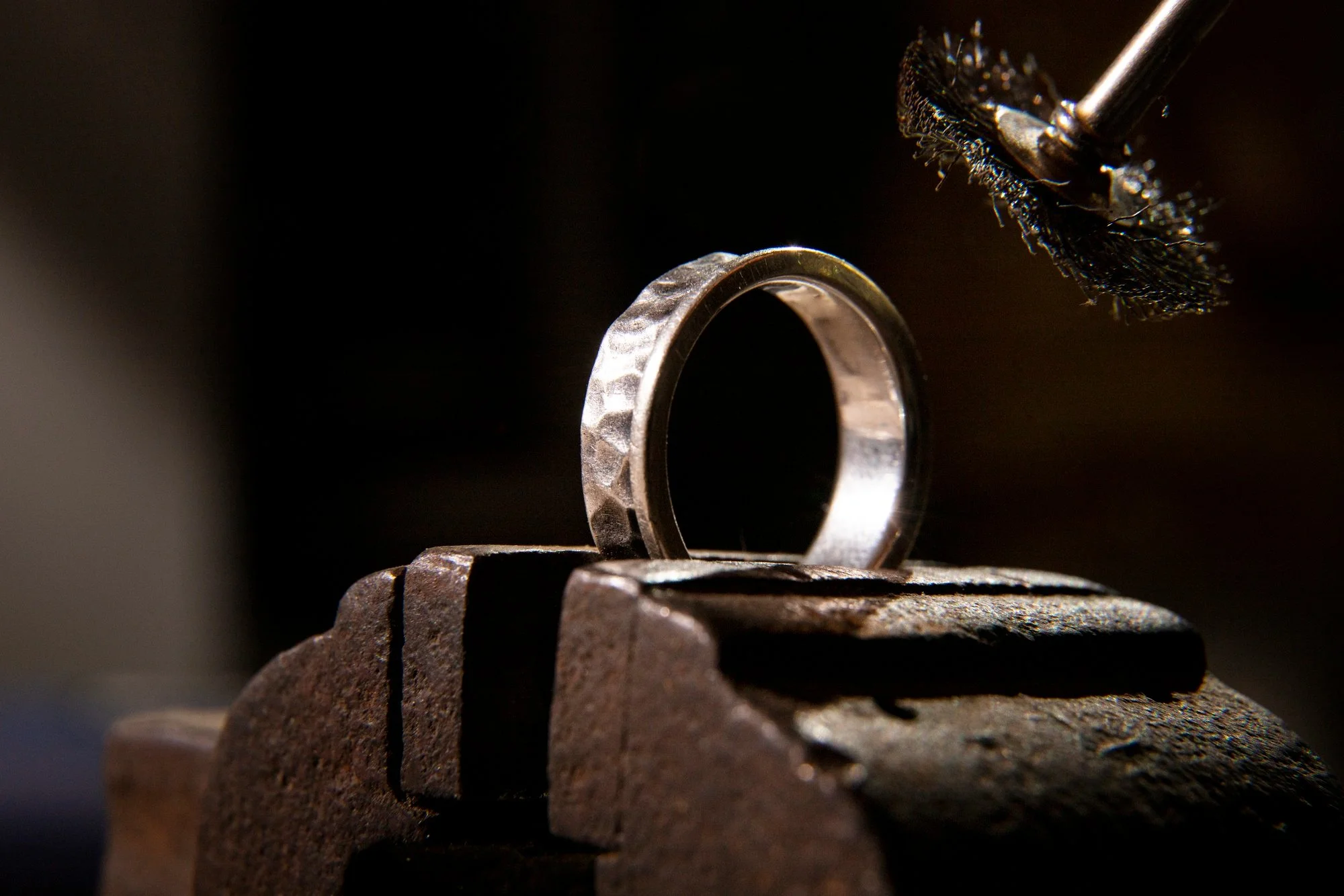 Close-up of a metal ring being shaped or engraved using a rotary tool with a small abrasive disc, set against a dark background.