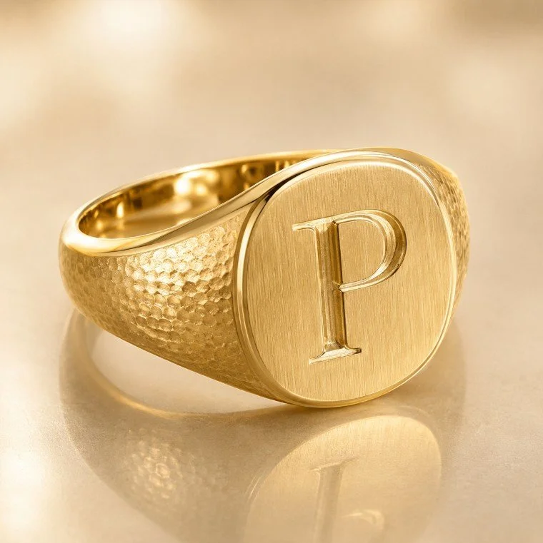 Close-up of a gold signet ring with a hammered texture on the band, featuring a letter 'P' engraved on a smooth circular face.
