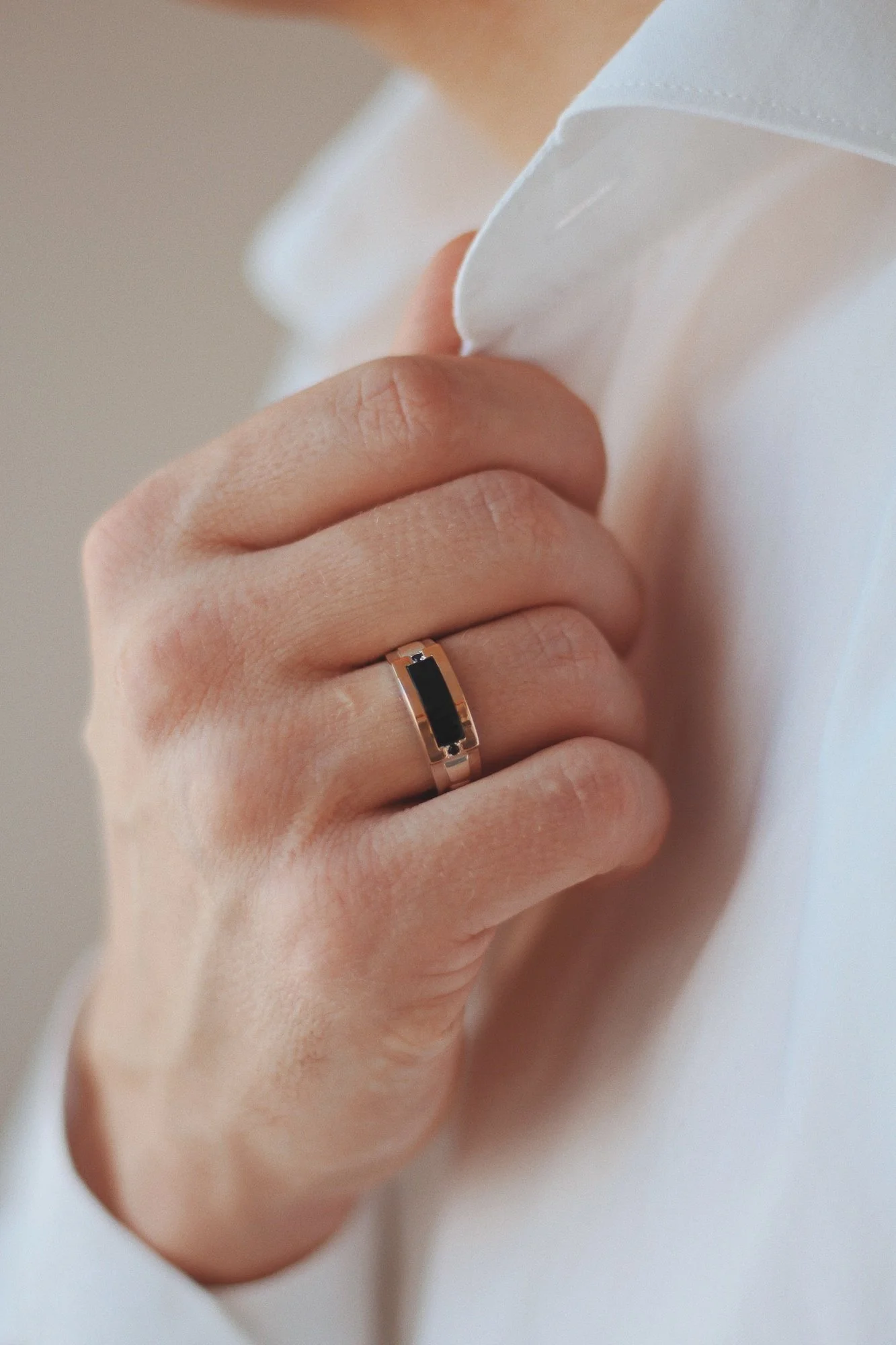 A close-up of a hand with a ring holding a white fabric, possibly a shirt or blouse.