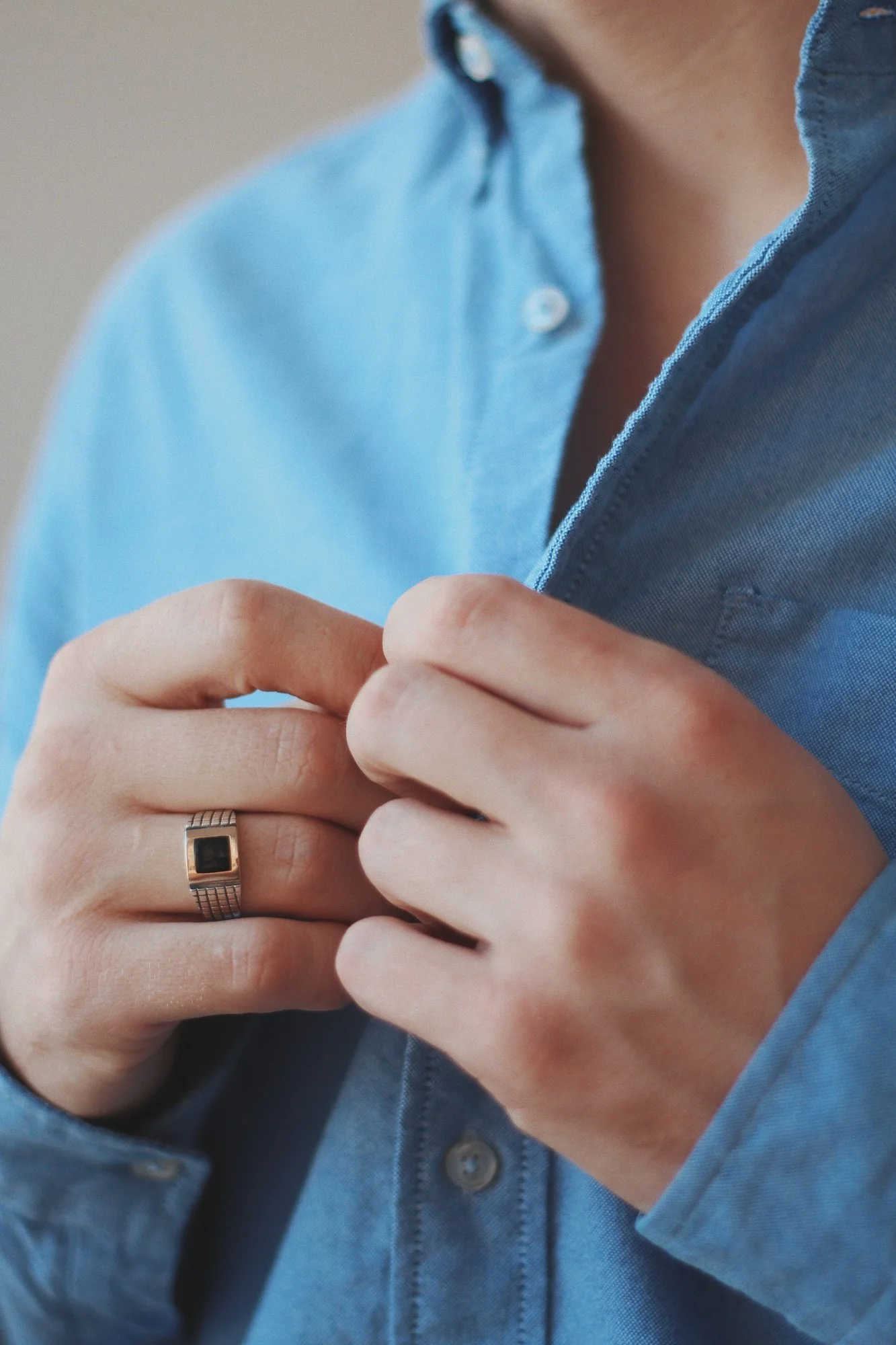 Person in a blue shirt buttoning their shirt, wearing a ring on their left hand.