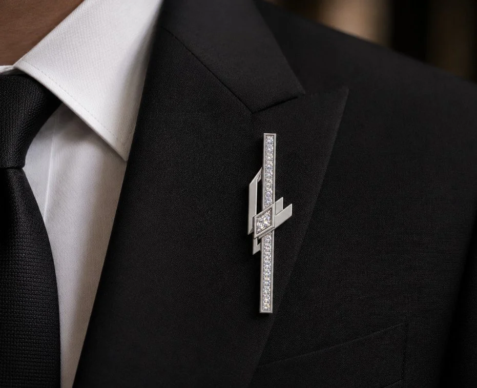 Close-up of a man wearing a black suit, white dress shirt, and black tie, with a decorative pin on his lapel featuring a geometric design and embedded rhinestones.