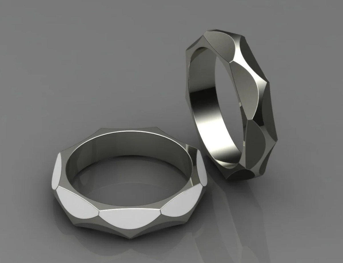Two custom-made rings with faceted, geometric designs on a gray surface. Available in gold, platinum, or silver.